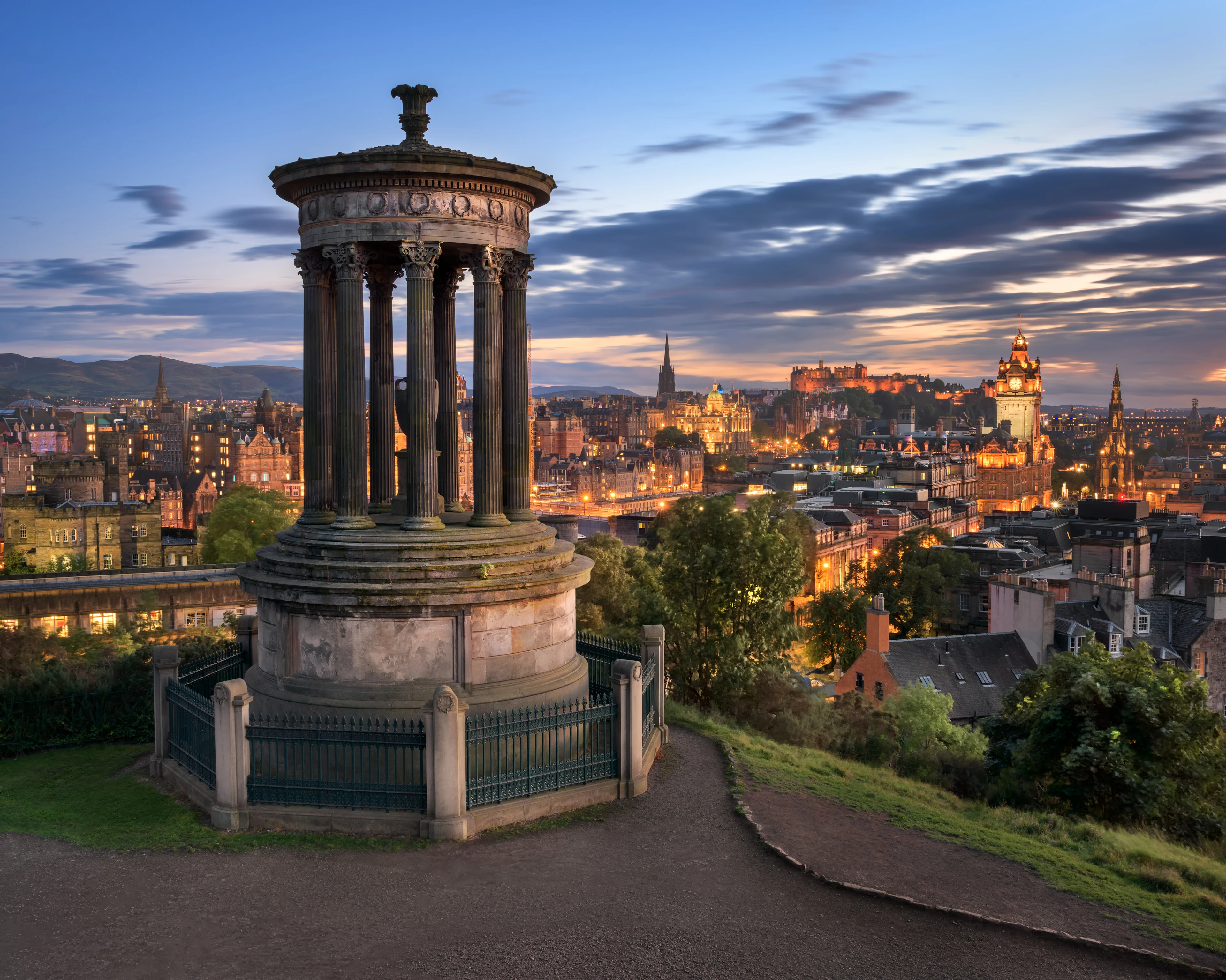 Näkymä Edinburghiin auringonlaskun aikaan Calton Hilliltä, Dugald Stewart -monumentti etualalla. Kaupungin historialliset rakennukset, Edinburghin linna ja Balmoral-hotelli voidaan nähdä taustalla valaistuna dramaattista taivasta vasten.