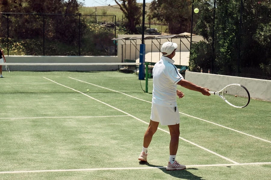 Man som spelar tennis med träd i bakgrunden