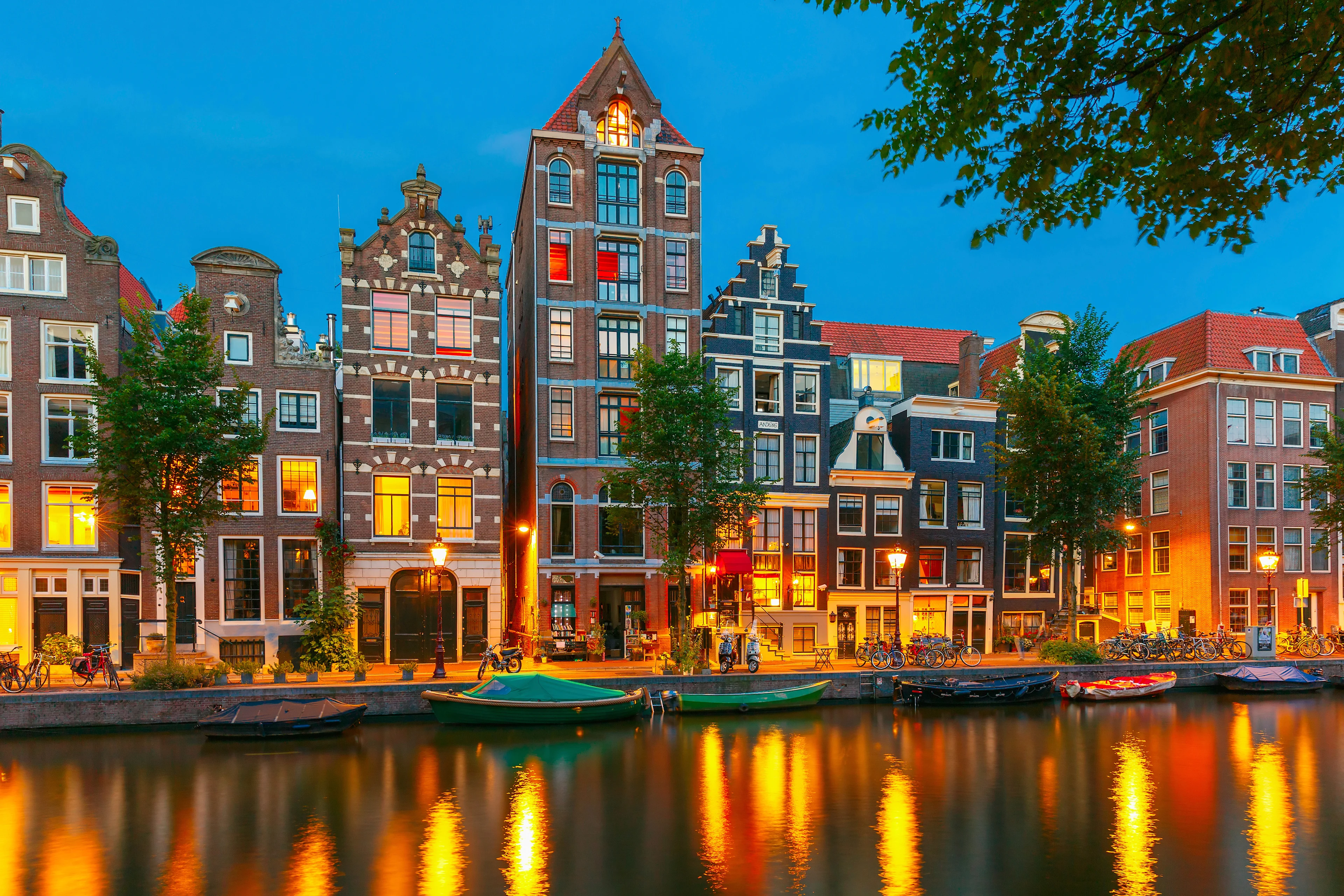 Upplysta kanalhus och båtar längs en kanal i Amsterdam i kvällsljus.
