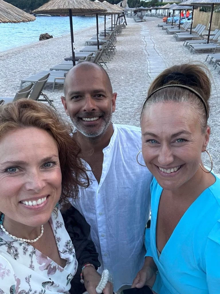 Kjersti, Kunal og Johanna på en strand med solsenger og parasoller i bakgrunnen.