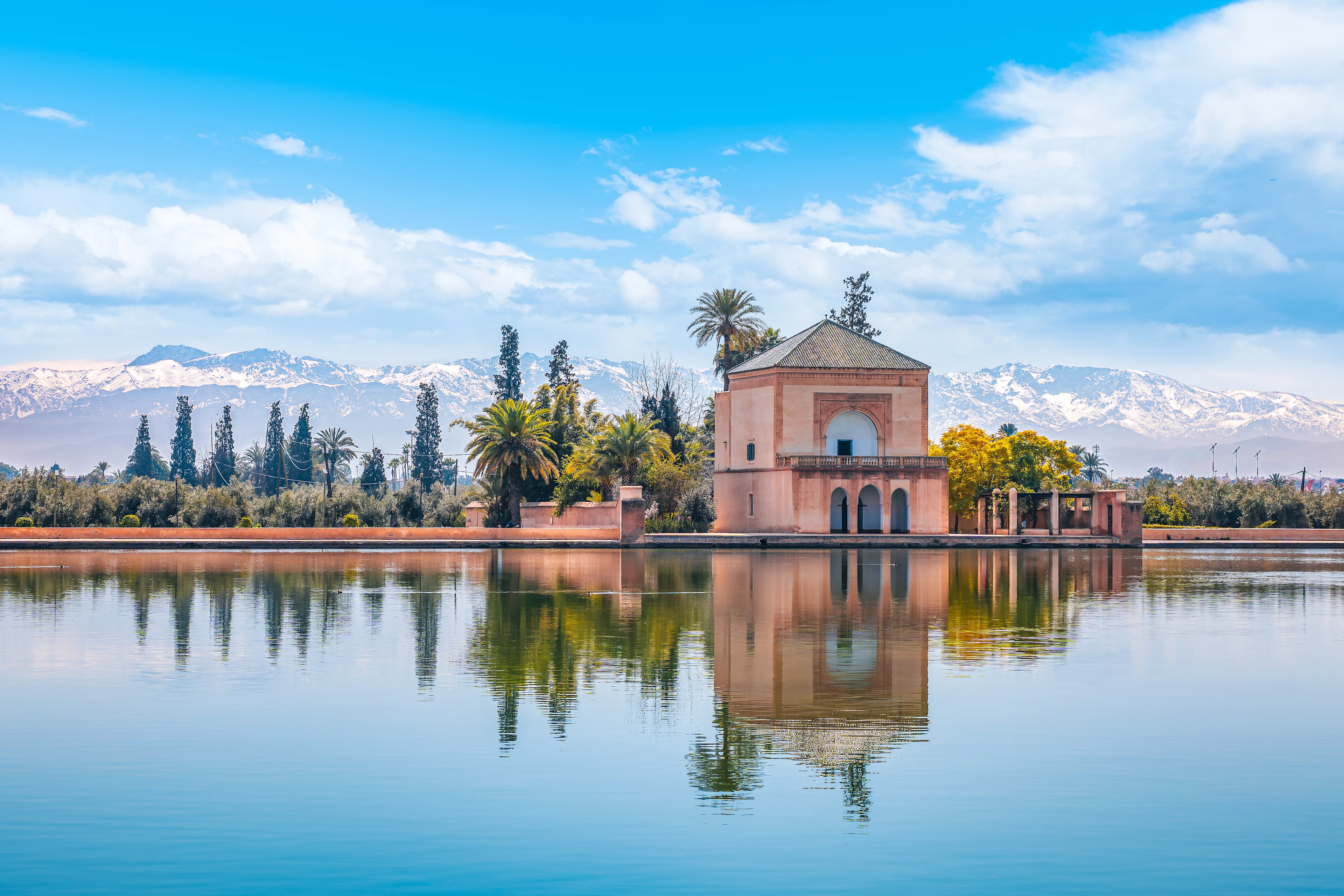 Paviljong vid en spegelblank damm i Marrakesh med Atlasbergen i bakgrunden.