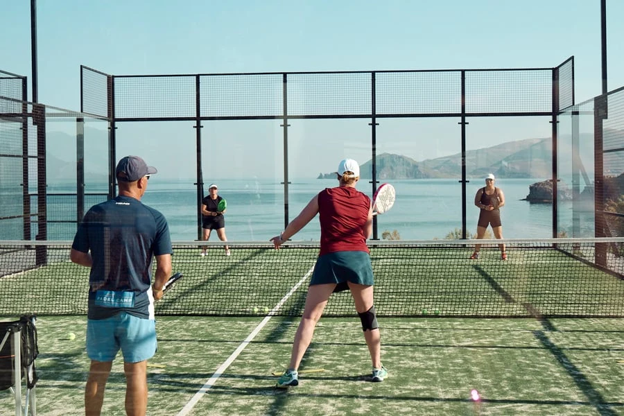 Folk spiller padel med havet i baggrunden