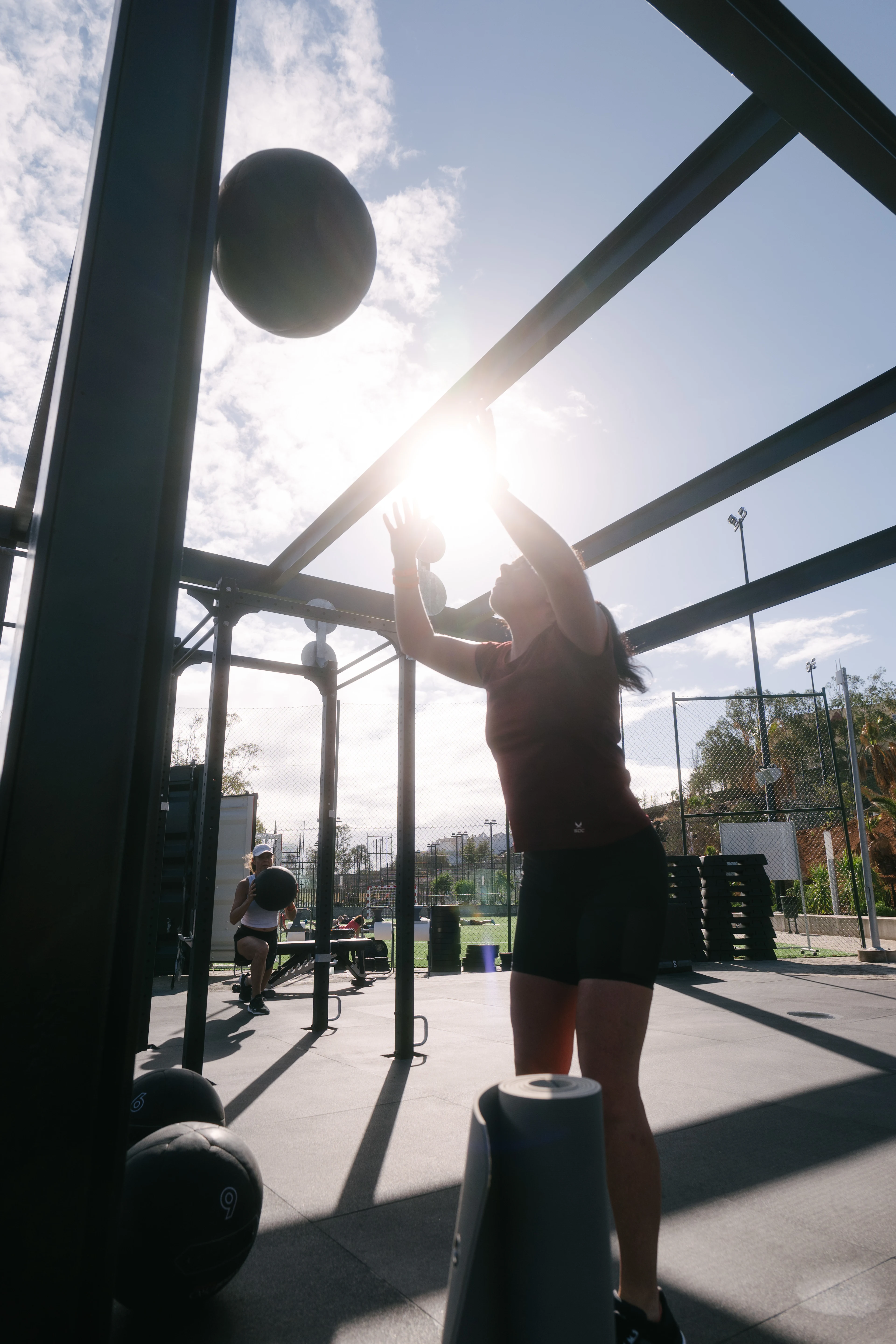 Dame som kaster en lærball ute i WOD-boxen med solen i bakgrunnen