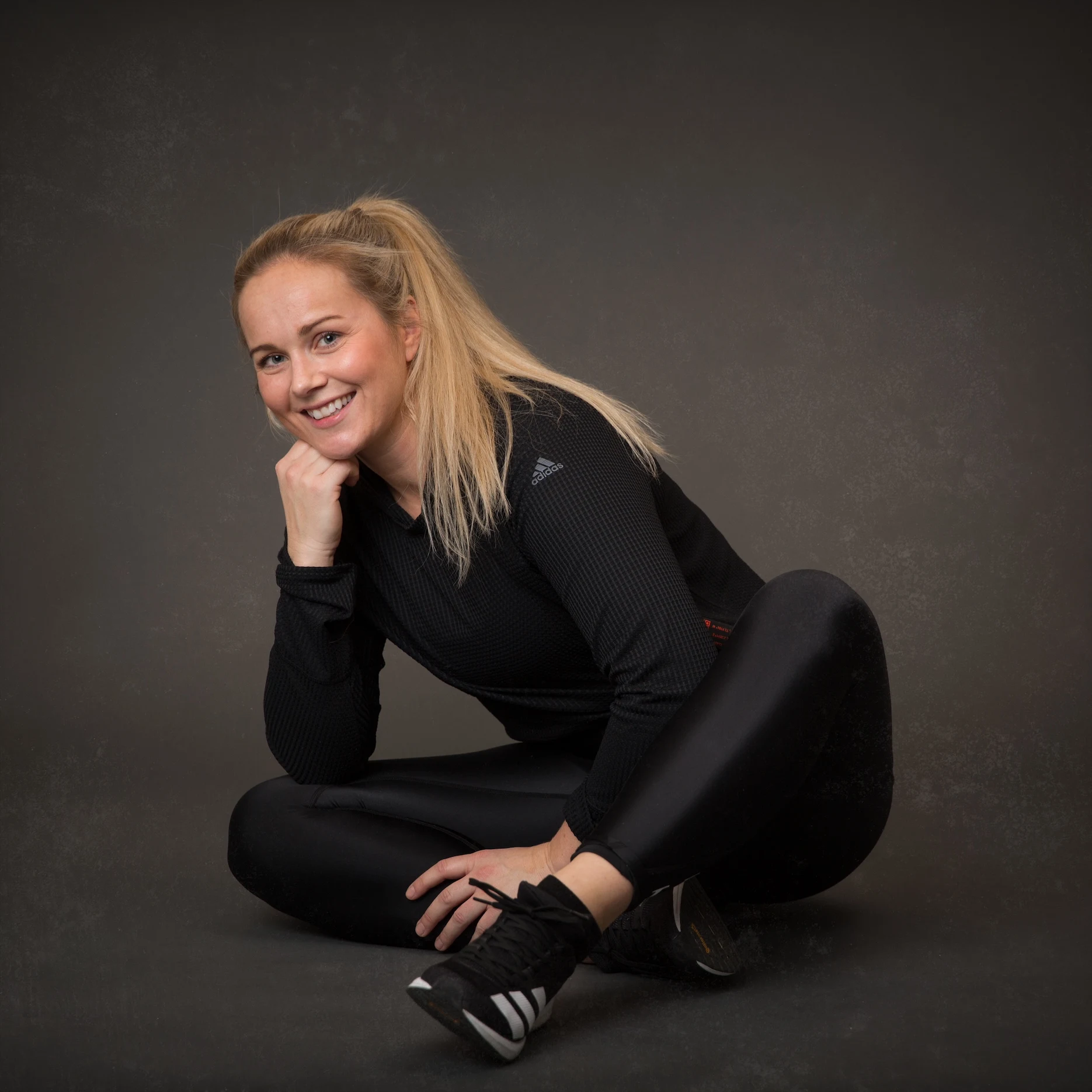 Ann Christin som sitter vendt mot kameraet og hviler hodet på den ene hånden med en albue på ket ene kneet, ikledd sort treningstøy.