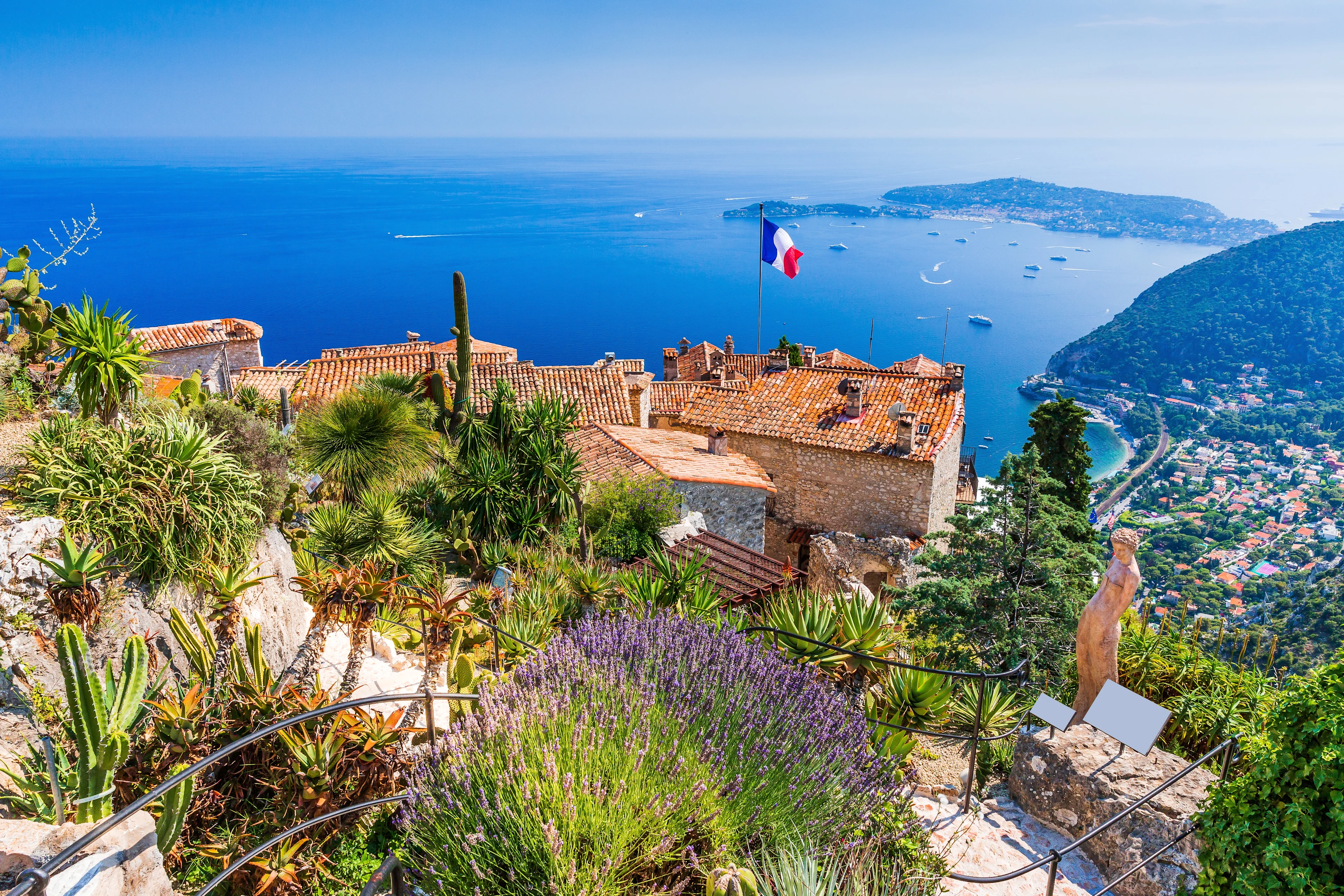 Utsikt från bergsbyn Èze på Franska rivieran med Medelhavet, terrakottafärgade hustak, grönskande trädgårdar och halvön Saint-Jean-Cap-Ferrat i bakgrunden.