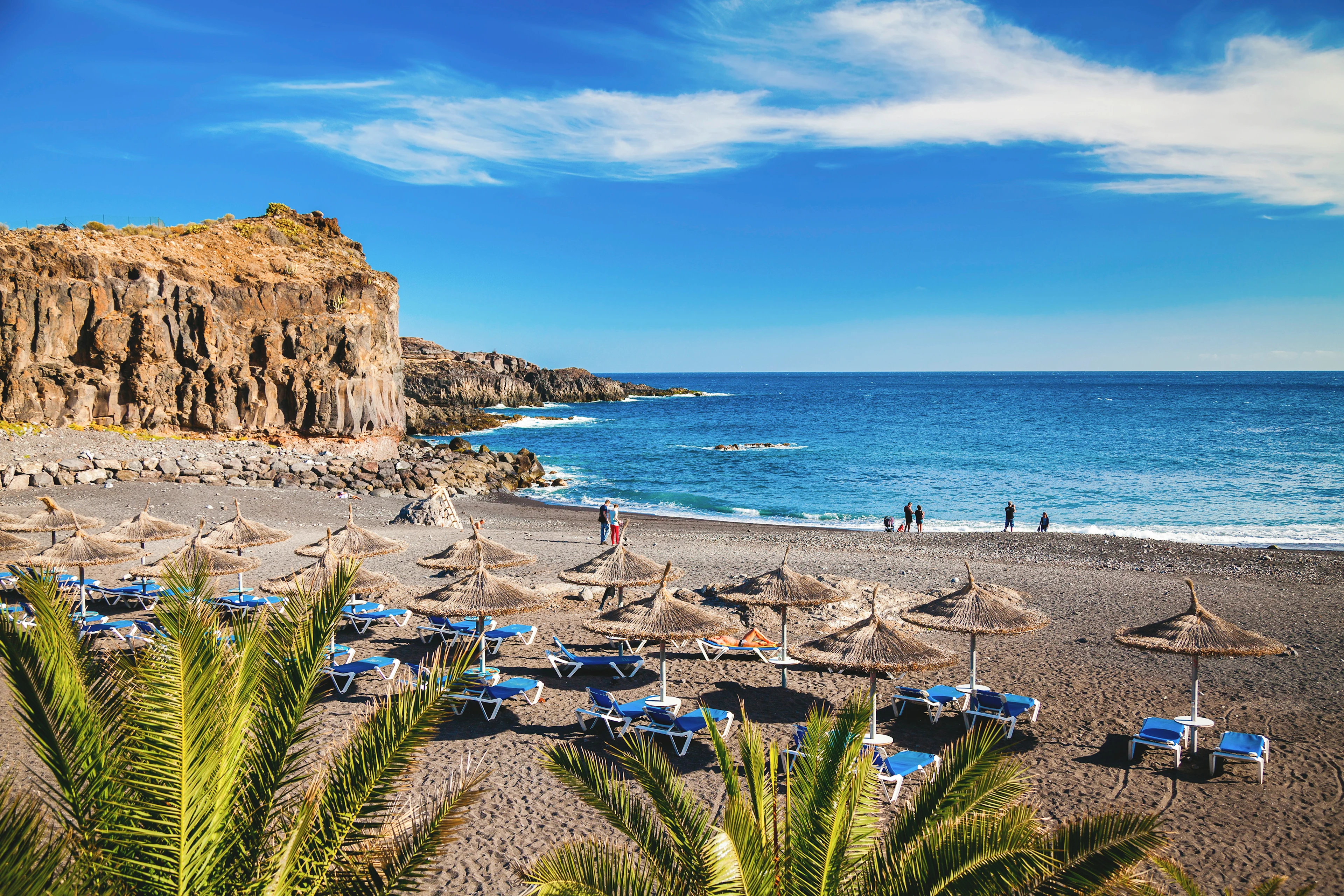 Vulkanstrand med svart sand, parasoller och klippor vid Atlantkusten på Teneriffa
