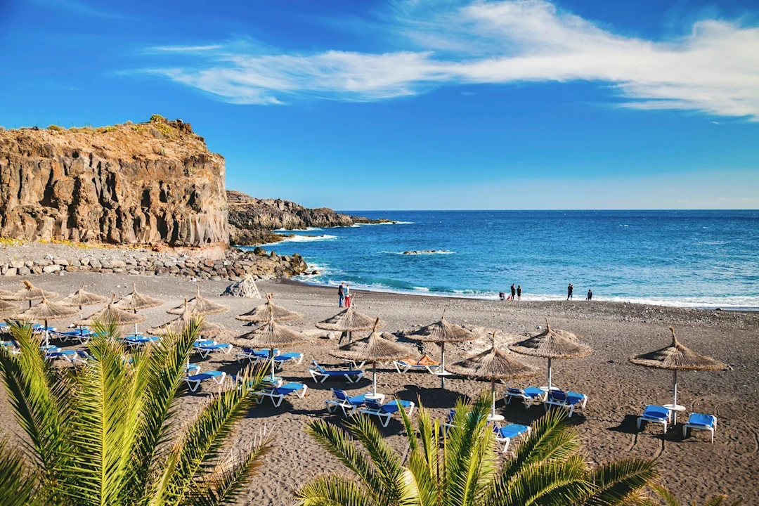 Vulkanstrand med svart sand, parasoller og klipper på Atlanterhavskysten av Tenerife.