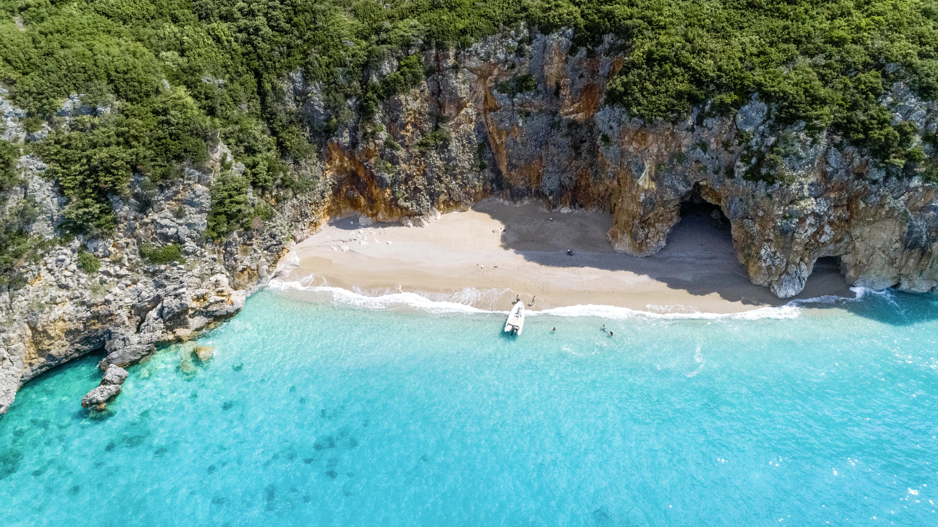 gömd sandstrand i Dhermi med berg omringandes med en båt intill stranden