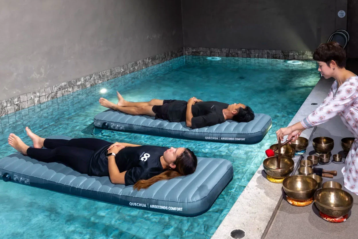 To deltakere flyter i et basseng under en session med krystallklangskåler