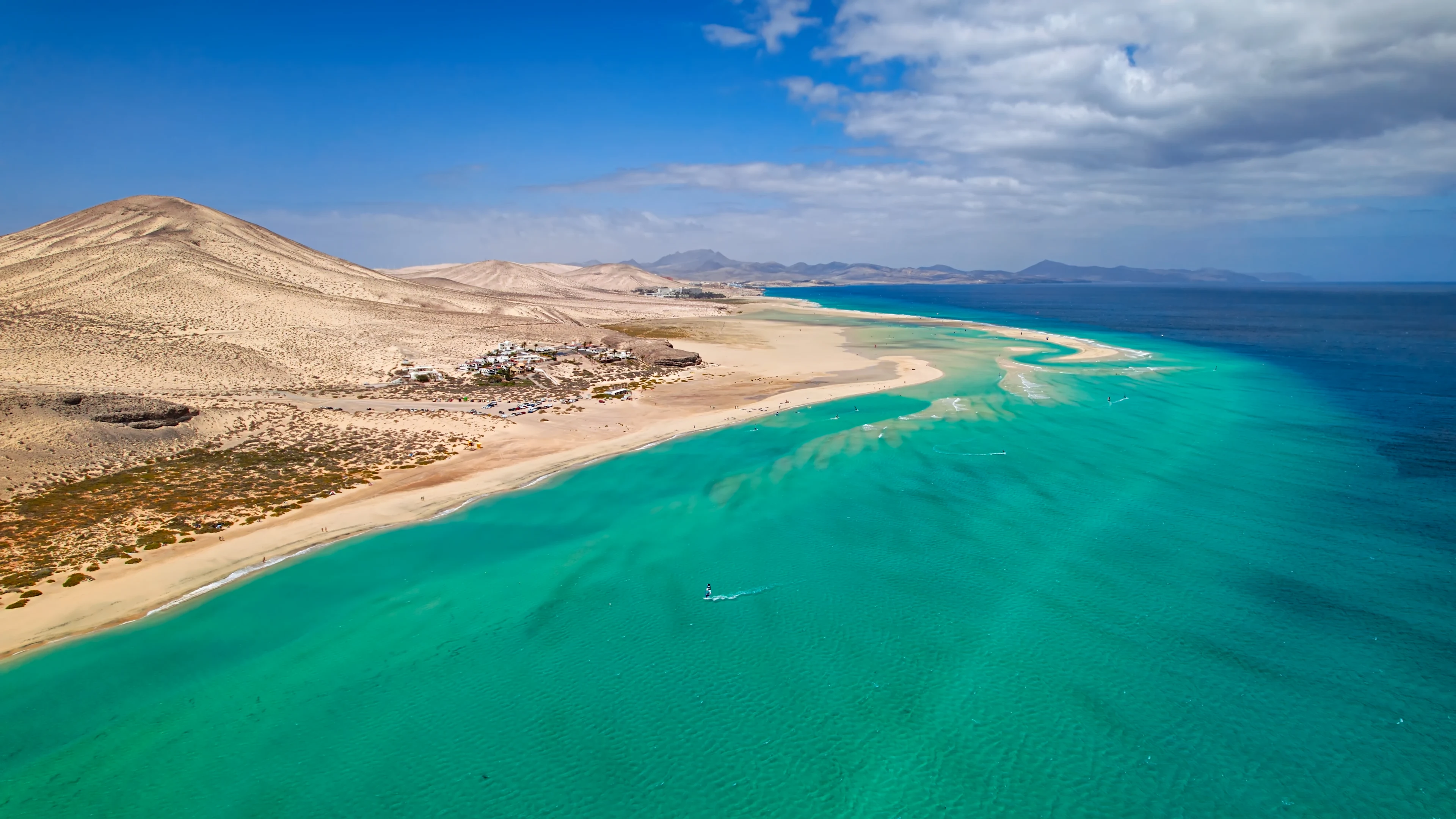 Luftfoto af lang sandstrand med turkisblåt hav og ørkenlandskab langs kysten