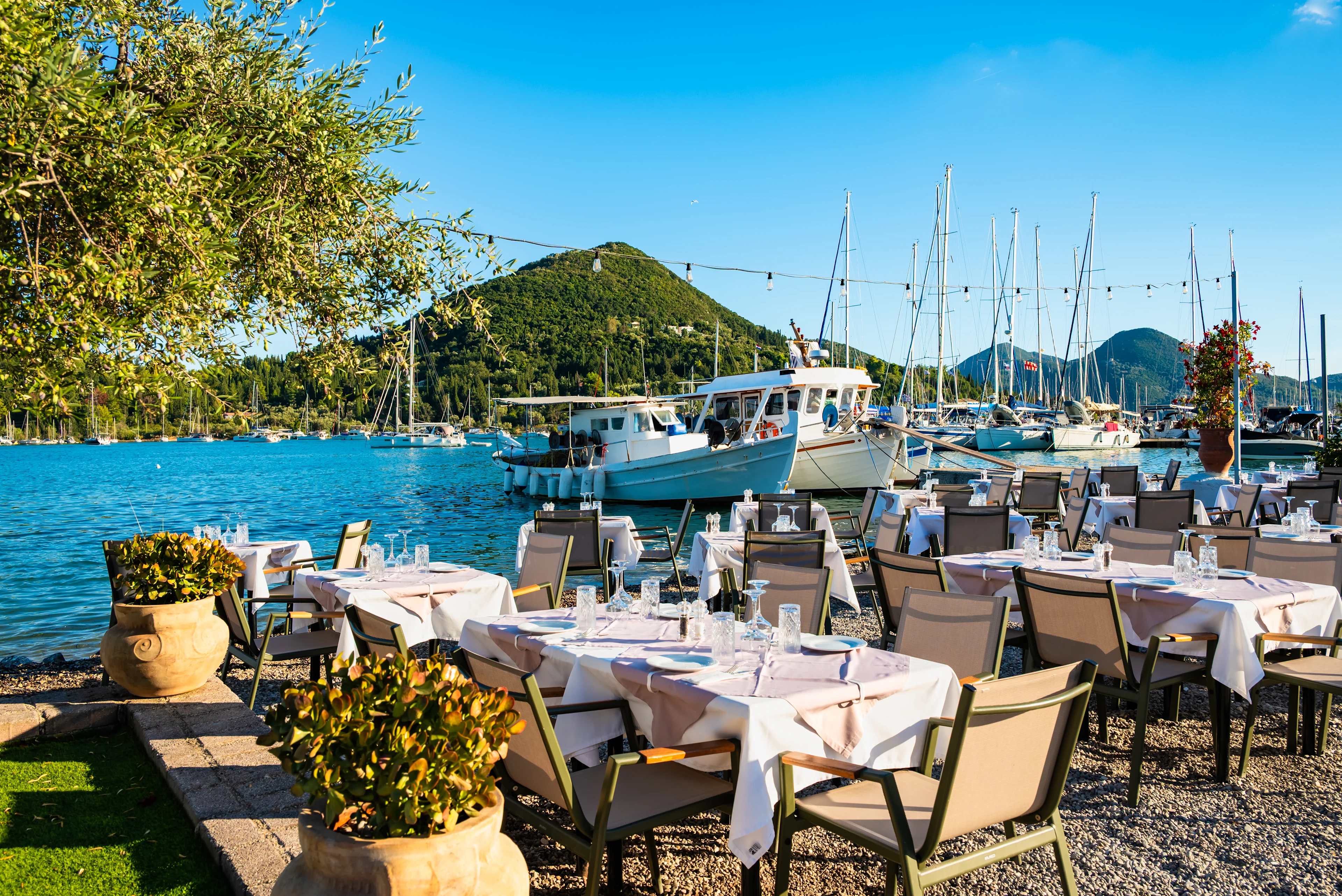 Uppdukade bord vid havet med båtar i bakgrunden i Nidri på Lefkas