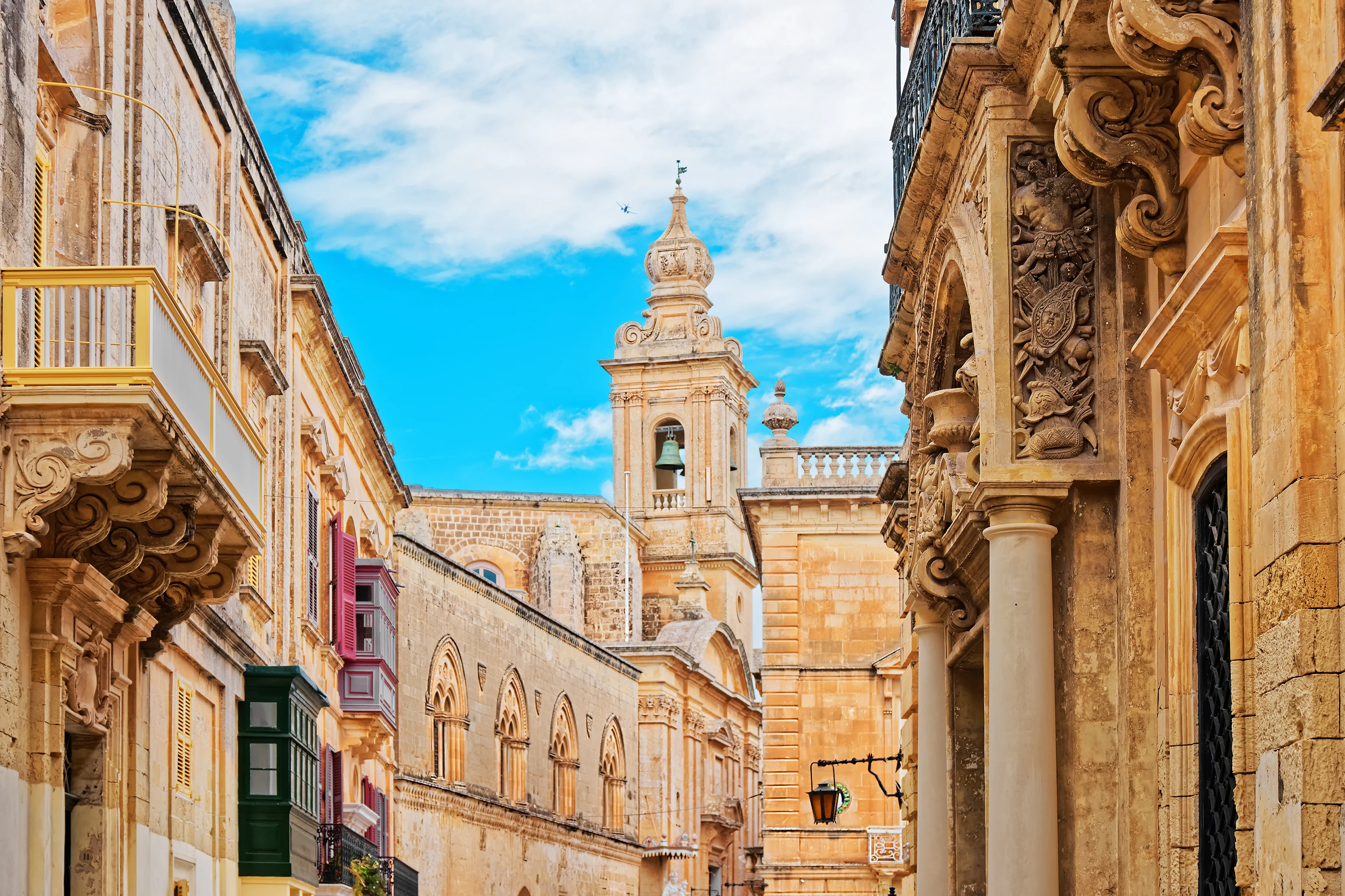 Historiske bygninger og smal gate i Mdina, Malta med den imponerende St. Paul's Cathedral i bakgrunnen.