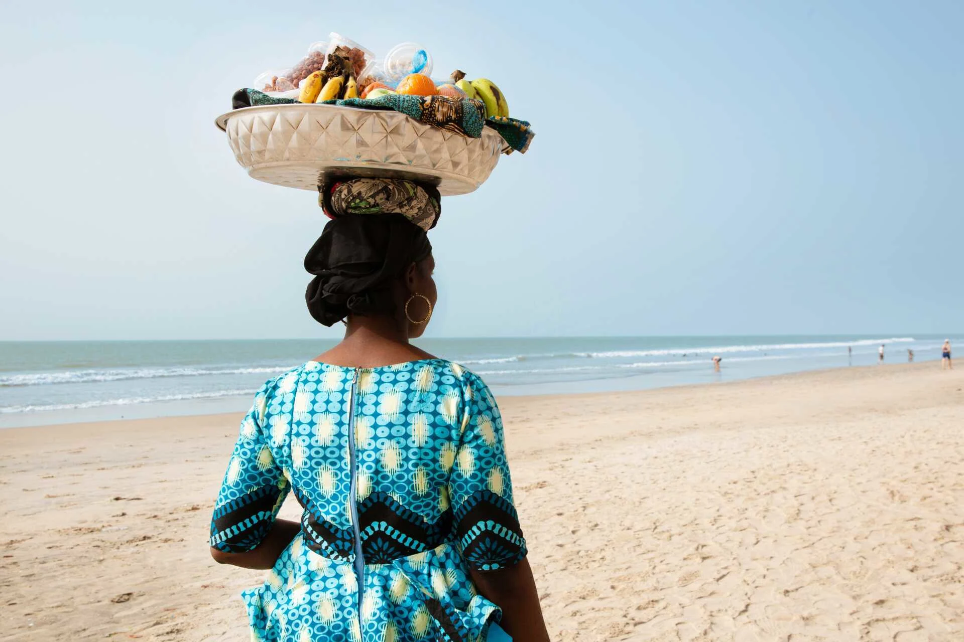 Kvinna som bär frukt på huvudet på en strand i Gambia