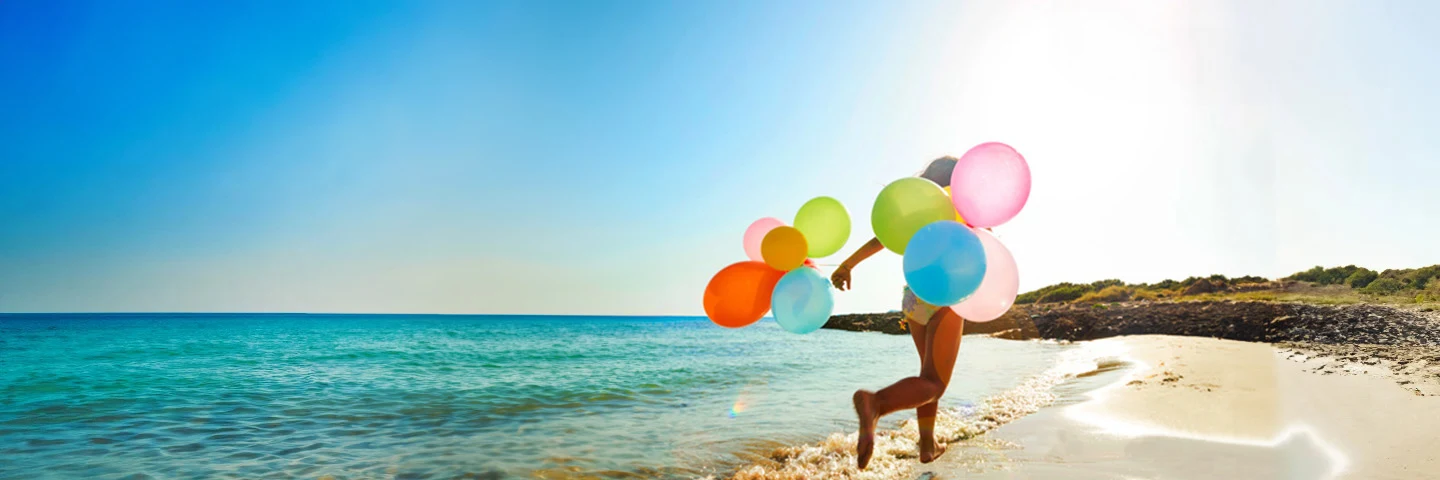 Liten jente løper langs stranden med mange ballonger