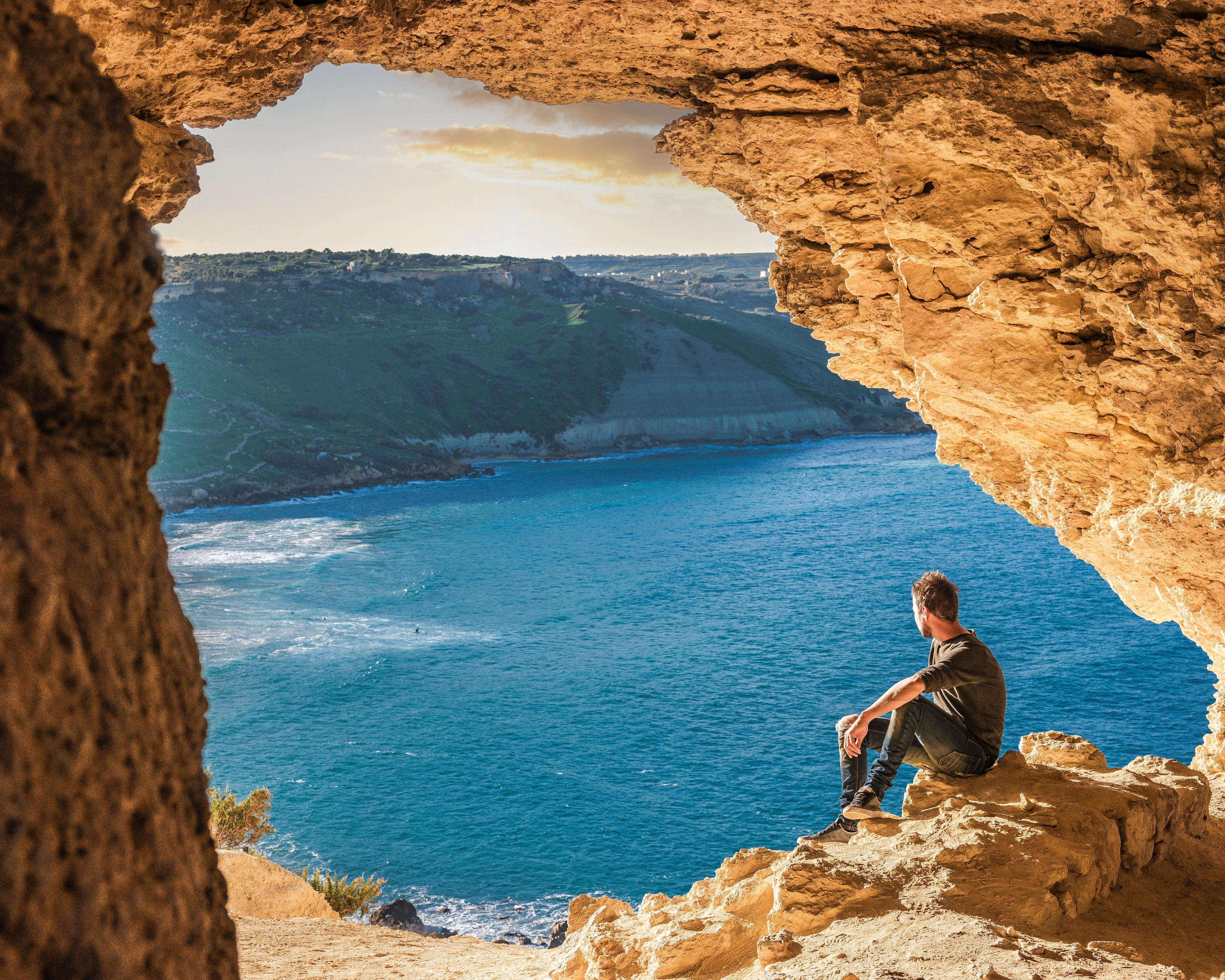 En ung man sitter i en grotta på Gozo och blickar ut över havet