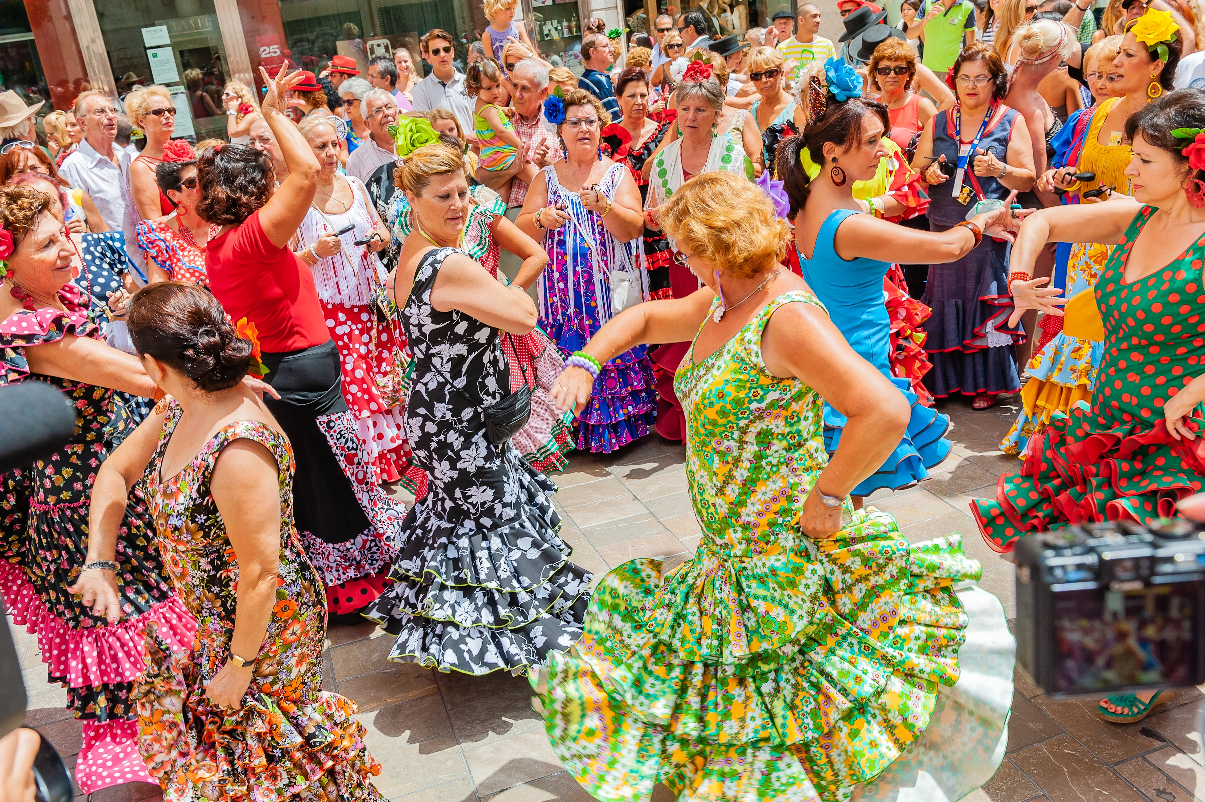 Kvinnor i färgglada flamencoklänningar dansar på Feria de Agosto inför en stor, festglad publik