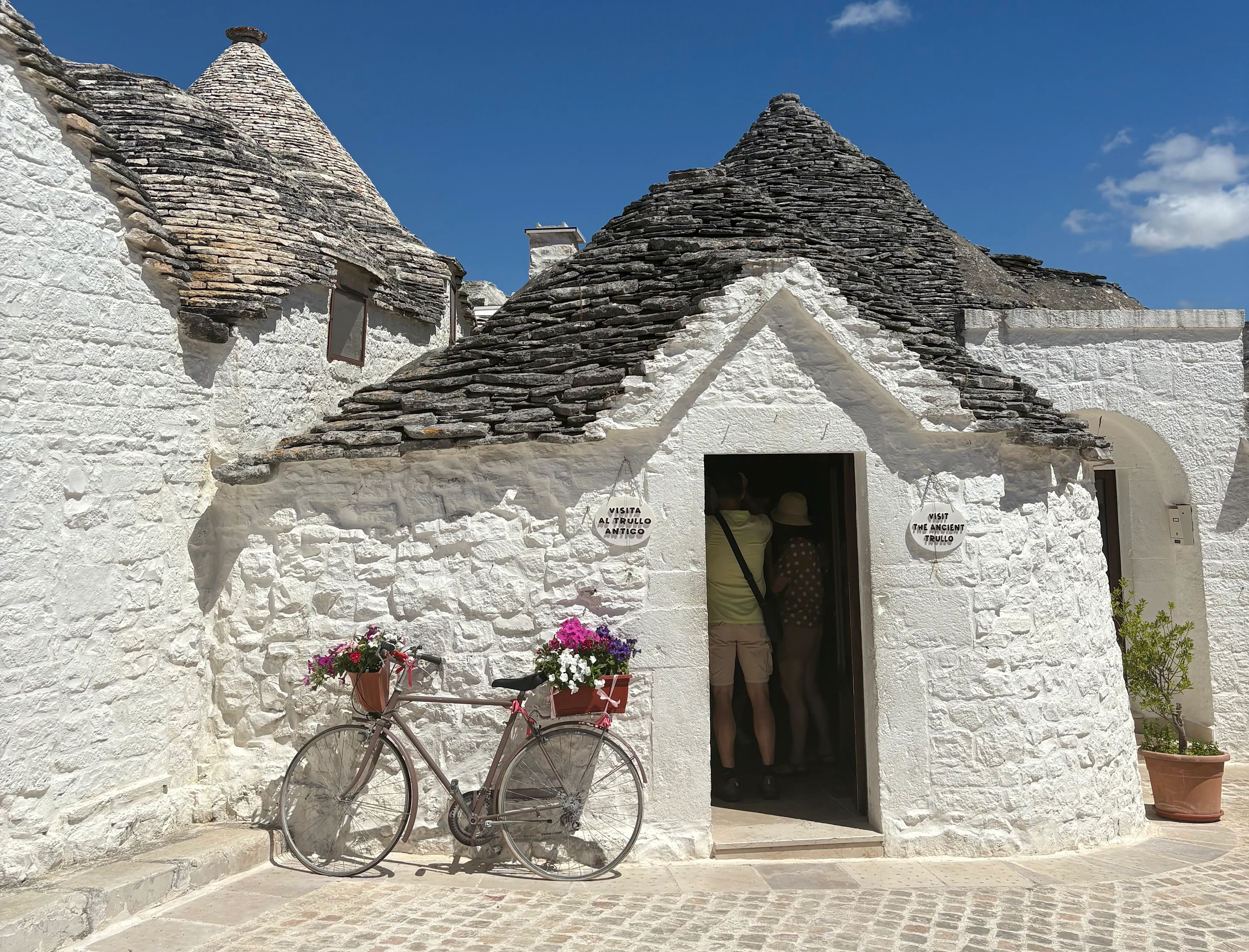 Traditionellt trullihus i Alberobello med vitkalkade väggar, konformat stentak och en blomsterdekorerad cykel utanför entrén.
