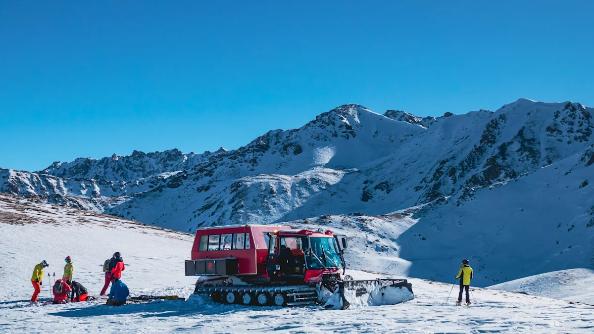 En röd pistmaskin står stilla i ett snötäckt bergslandskap medan flera personer med utrustning förbereder sig i klar och solig miljö.