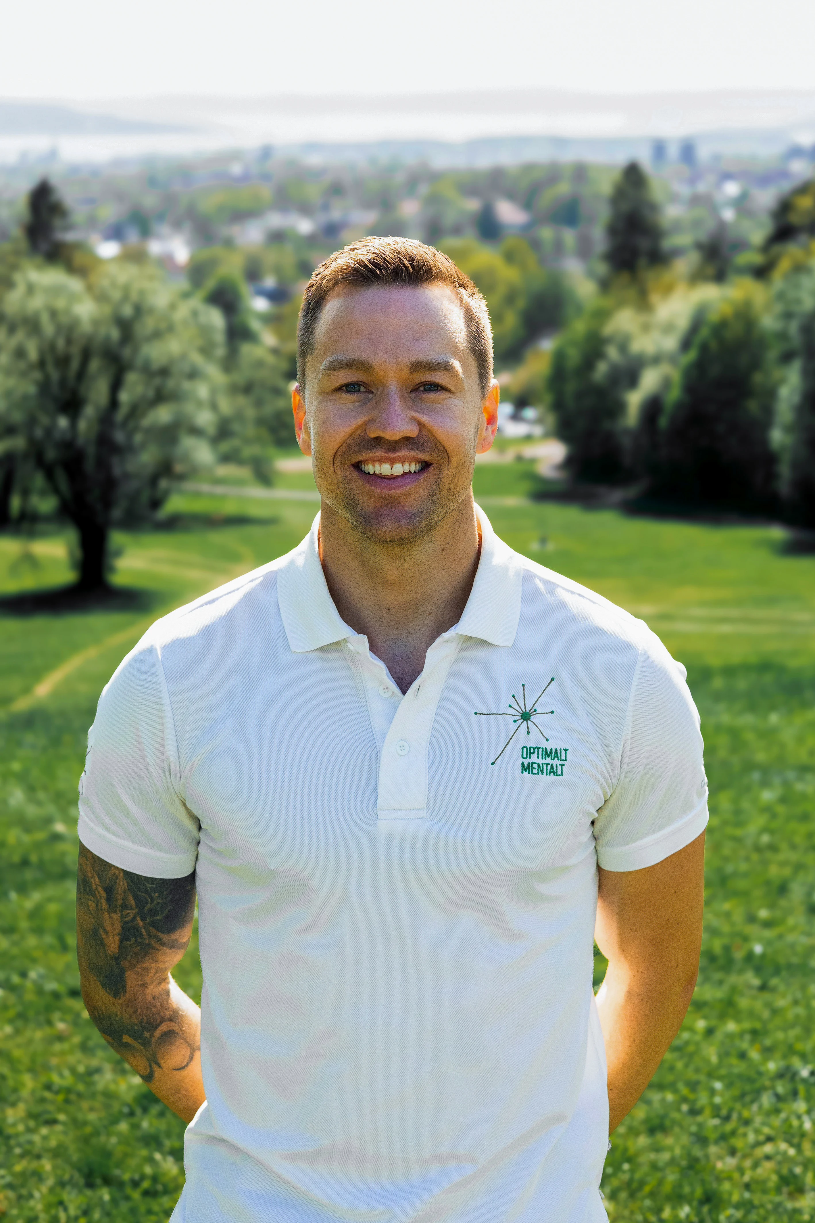 Profilbilde av Hallgeir som står ute på en gressplen i kledd hvit piquet t skjorte.