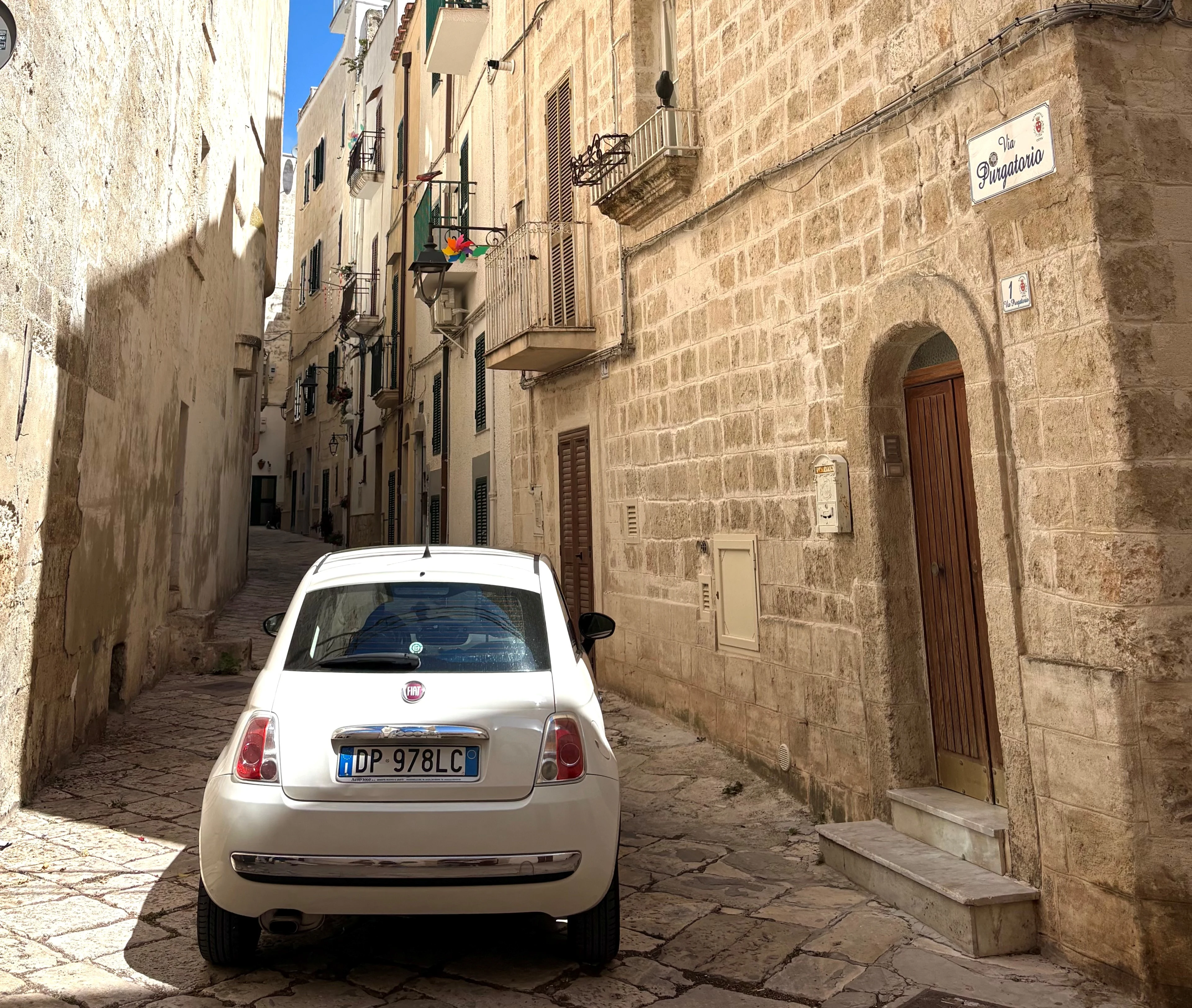 Smal stenbelagd gränd med en vit bil parkerad mellan historiska byggnader i Italien.
