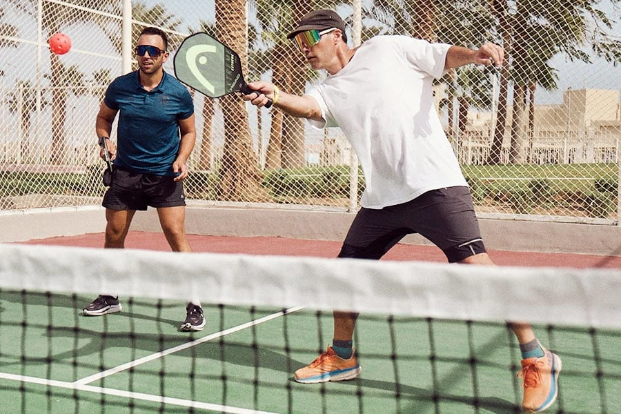 Två män som spelar pickleball med palmer i bakgrunden 