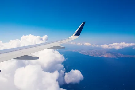 Utsikt över flygplansvinge, vita moln och en bergig grekisk ö från ett flygplansfönster