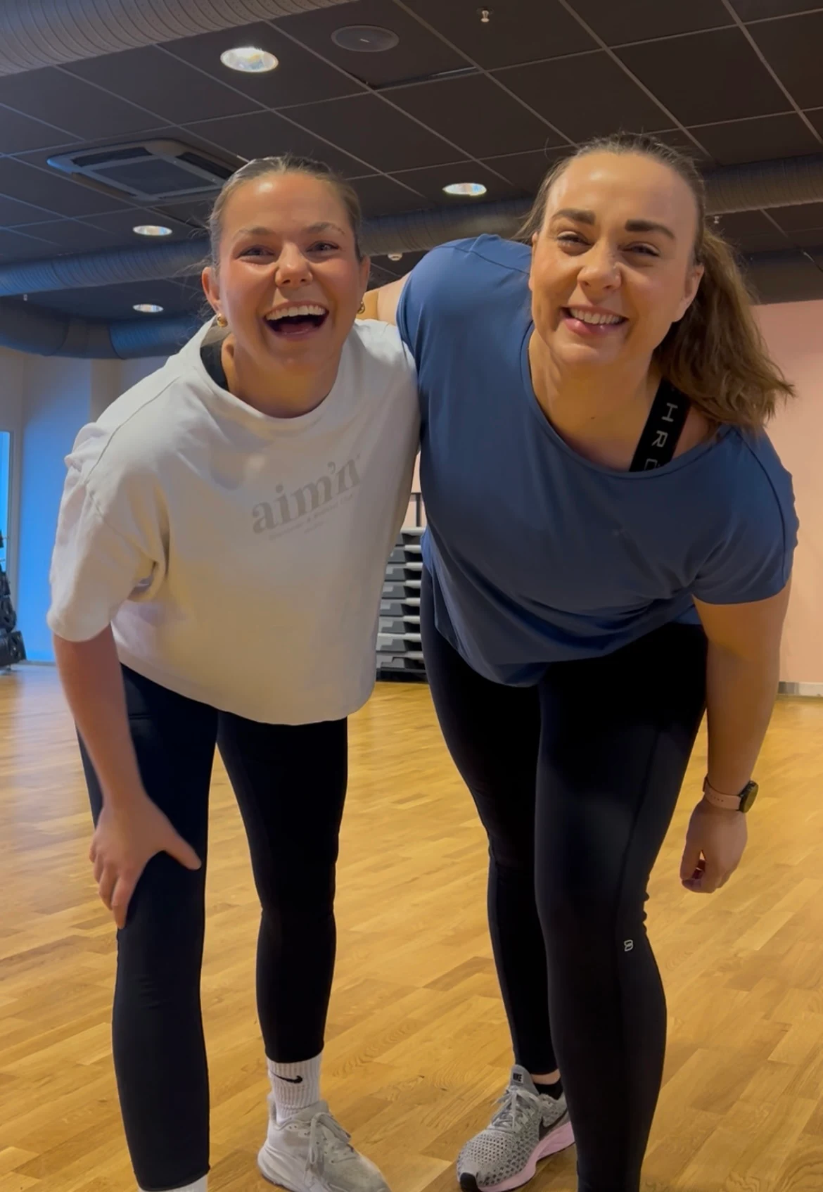Camilla kledd i hvit t skjorte og Lotte kless i blå t skjorte, står i en treningshall og ser mot kamera