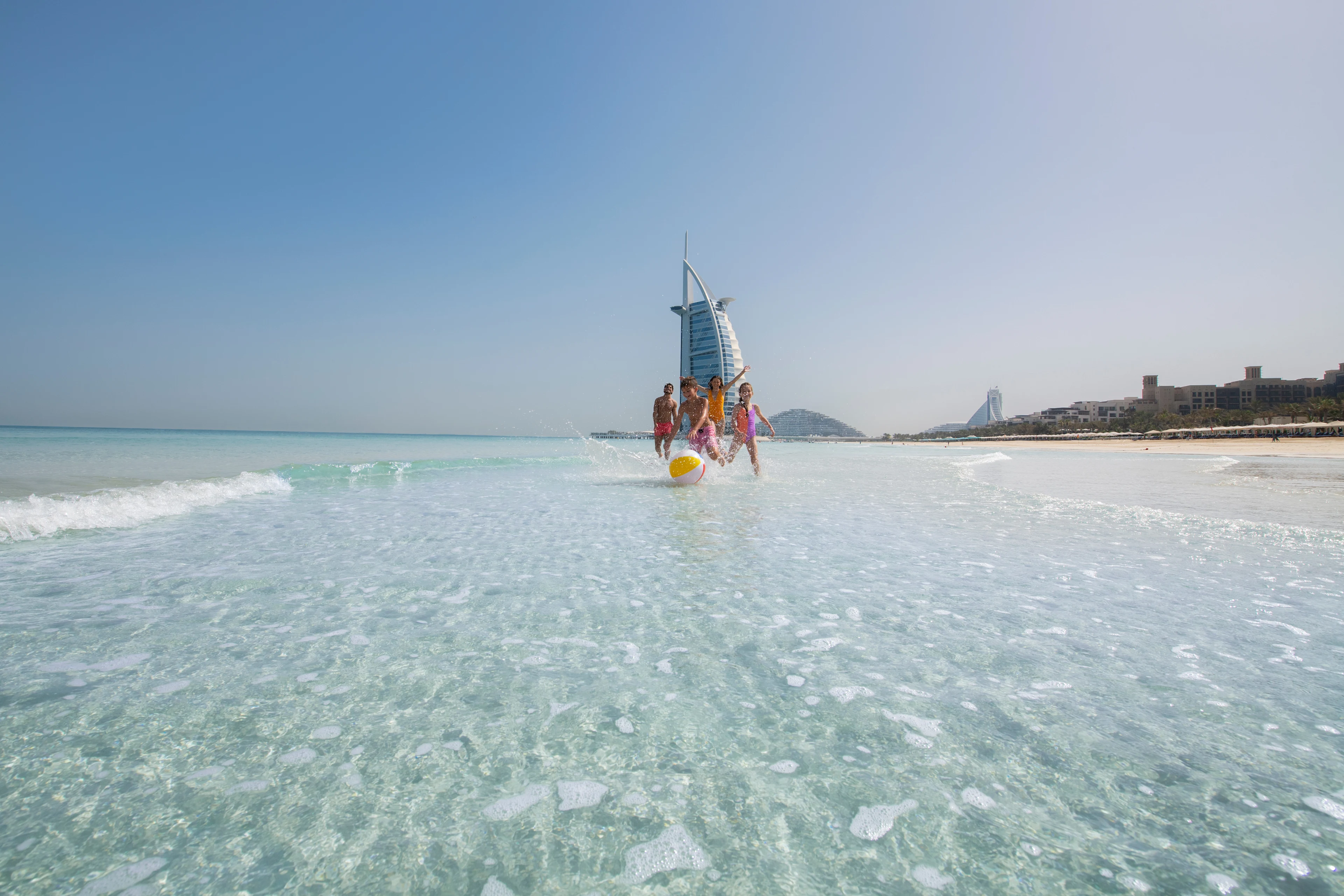 En familj som leker i vattnet på stranden vid Burj Al Arab