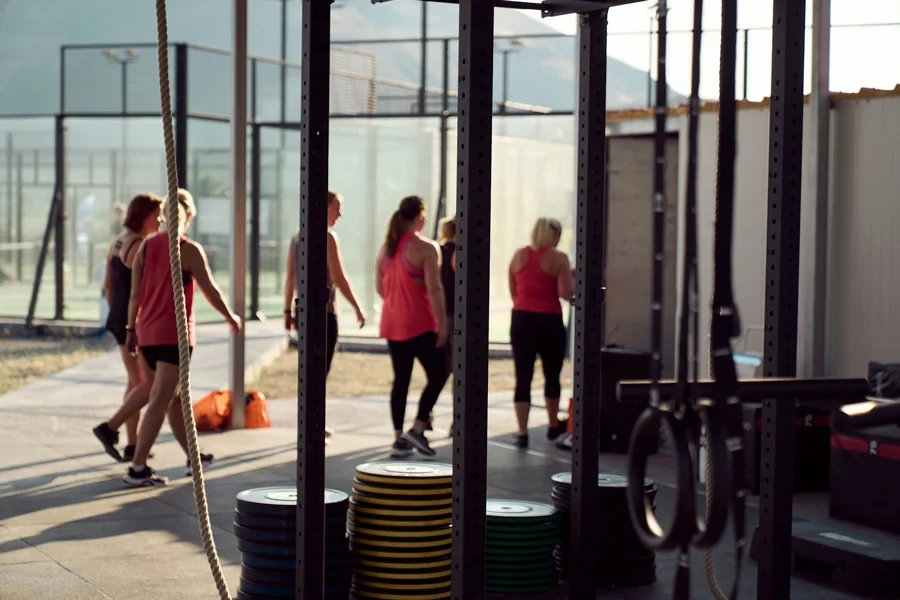 Träningsanläggning med redskap i förgrunden och padelbanor banor i bakgrunden med människor som går förbi
