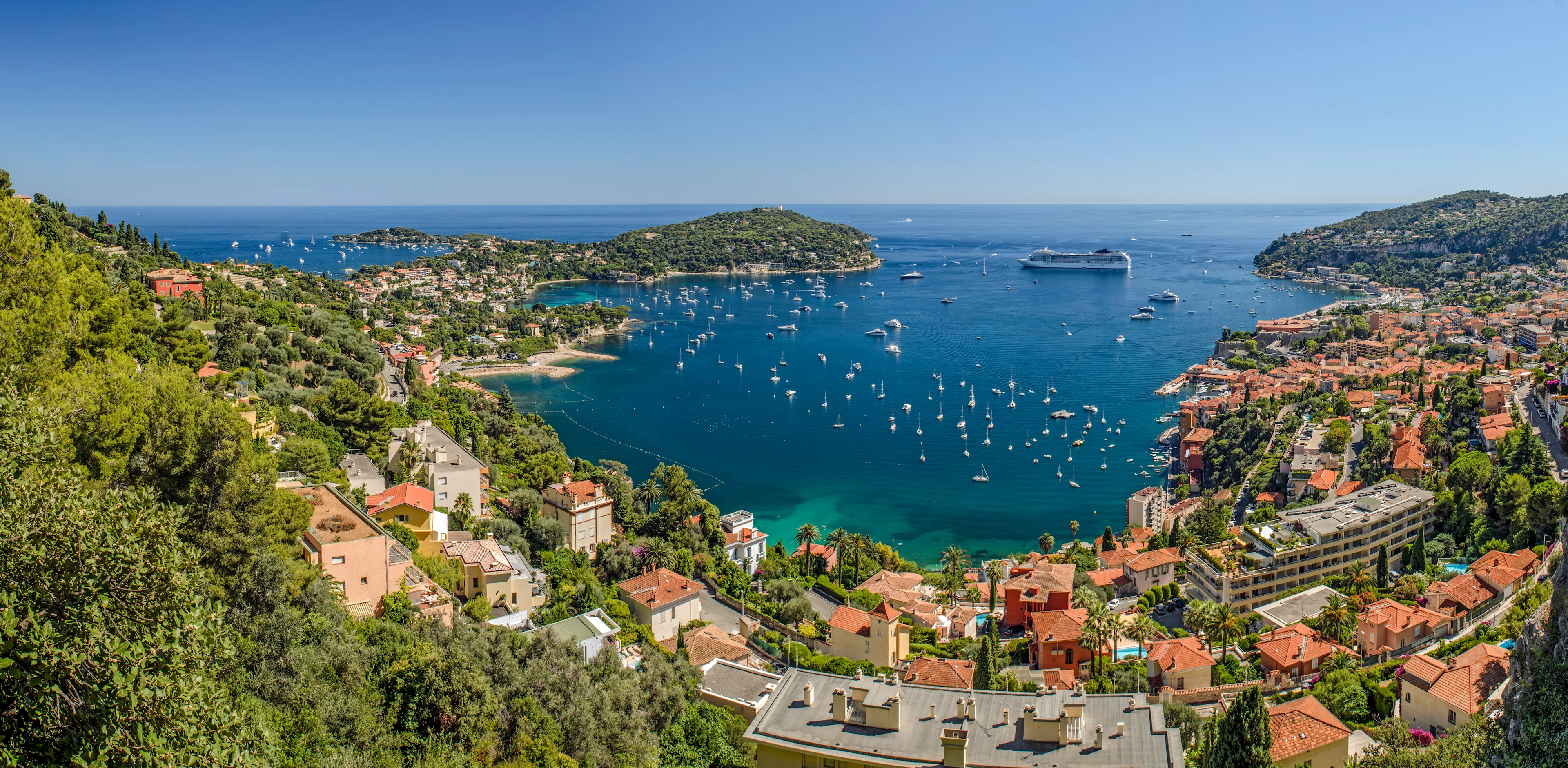 Utsikt över Villefranche-sur-Mer på Franska rivieran med turkost hav, segelbåtar i bukten och färgglada hus längs kusten.