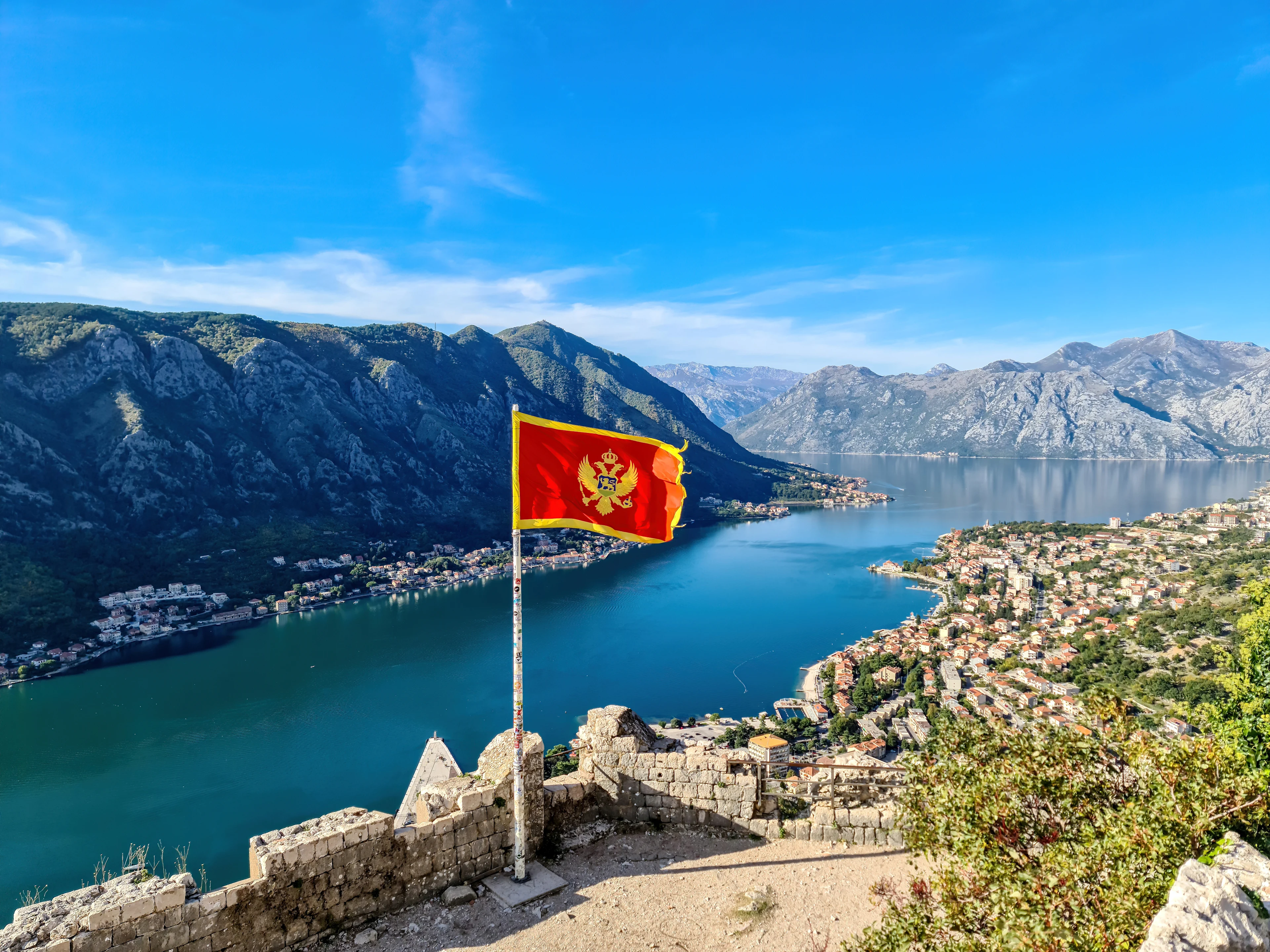 Montenegros flagga som fladdrar i vinden, med hav och berg i bakgrunden.