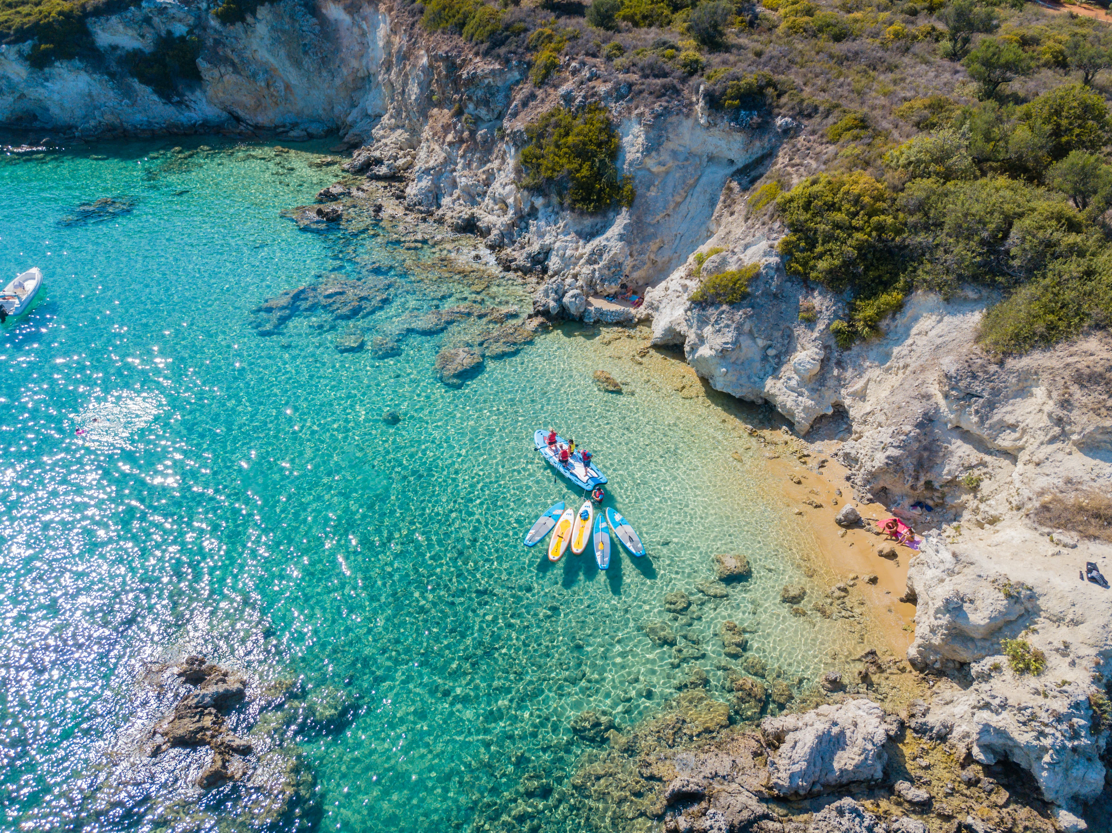Turkis bugt på Kreta med klart vand, klipper og surfbrætter tæt på kysten.