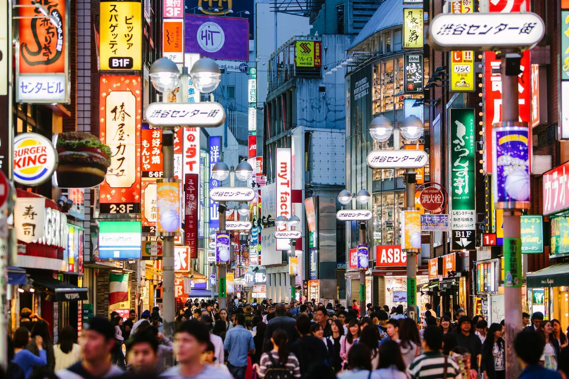 Folktät shoppinggata i Tokyo med neonbelysta skyltar, butiker och restauranger som lyser upp stadskvällen.