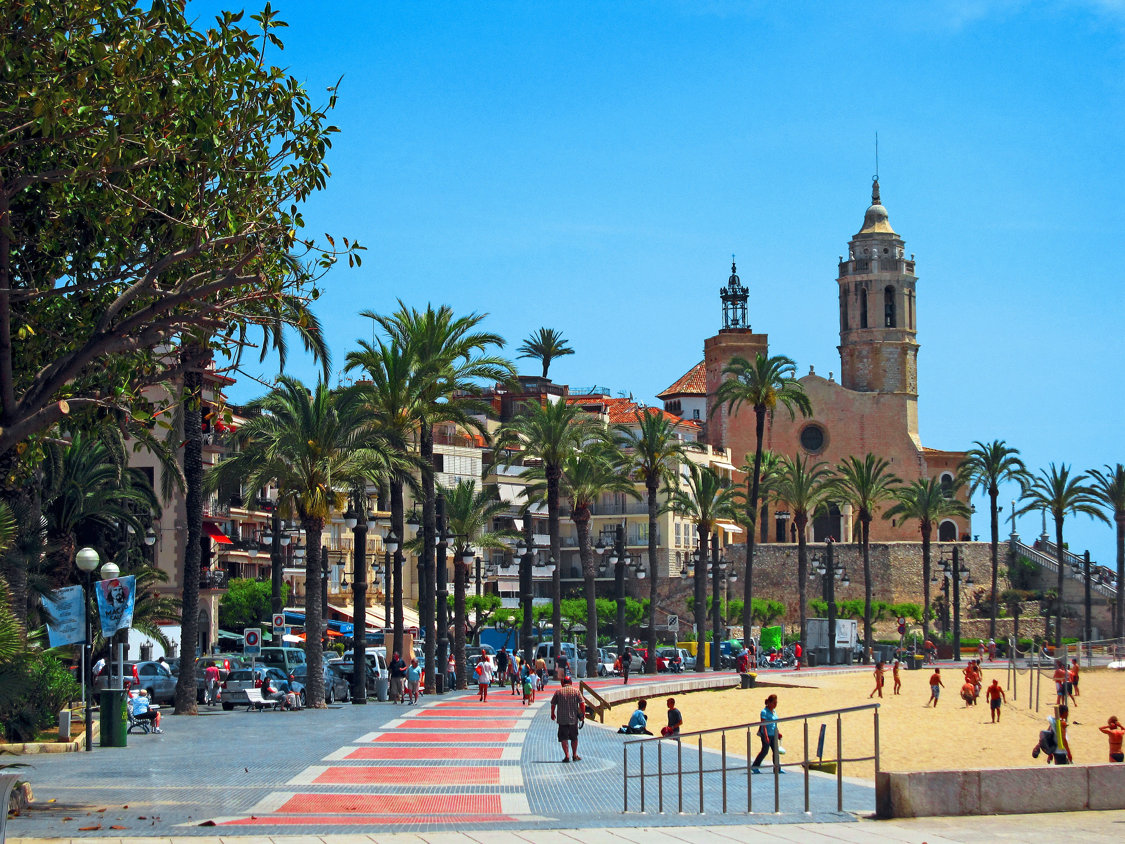 Utsikt over strandpromenaden, palmer og en kirke i Sitges