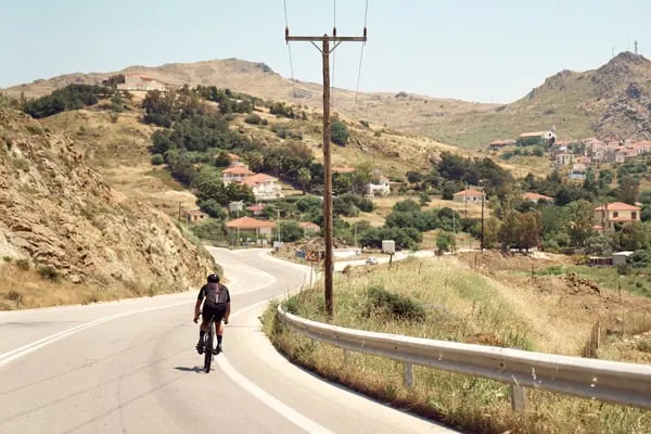 cyklist på landsväg med hus och berg i bakgrunden