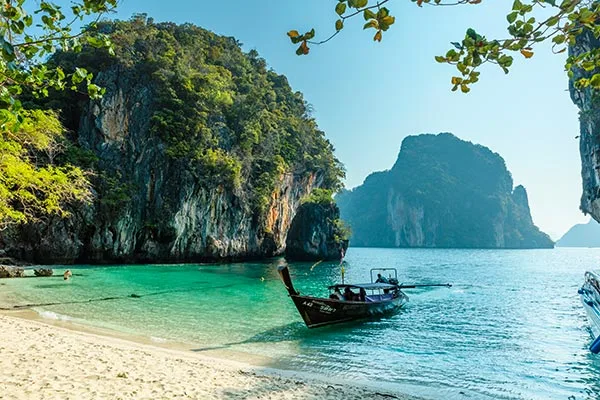 En typisk thailandsk båt ligger inntil idyllisk strand i en vakker bukt