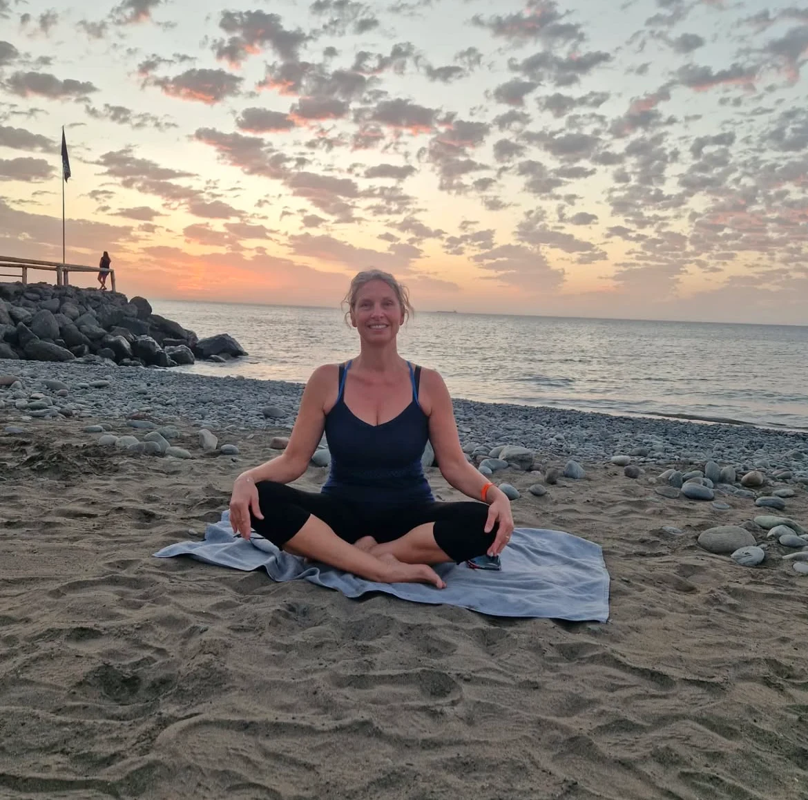 Gabriela Hansen sitter på et håndkle på en strand med beina i kors 