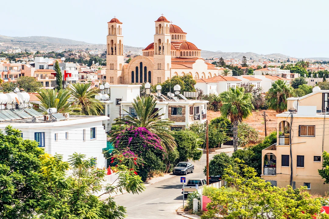 Utsikt över Paphos med kyrkobyggnad, palmer och bostadshus i solljus.