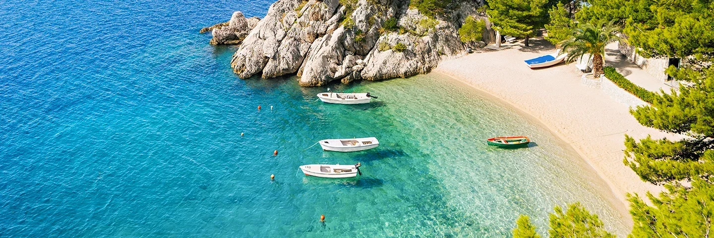 Vakker liten strand med småbåter som dupper i det krystallklare vannet