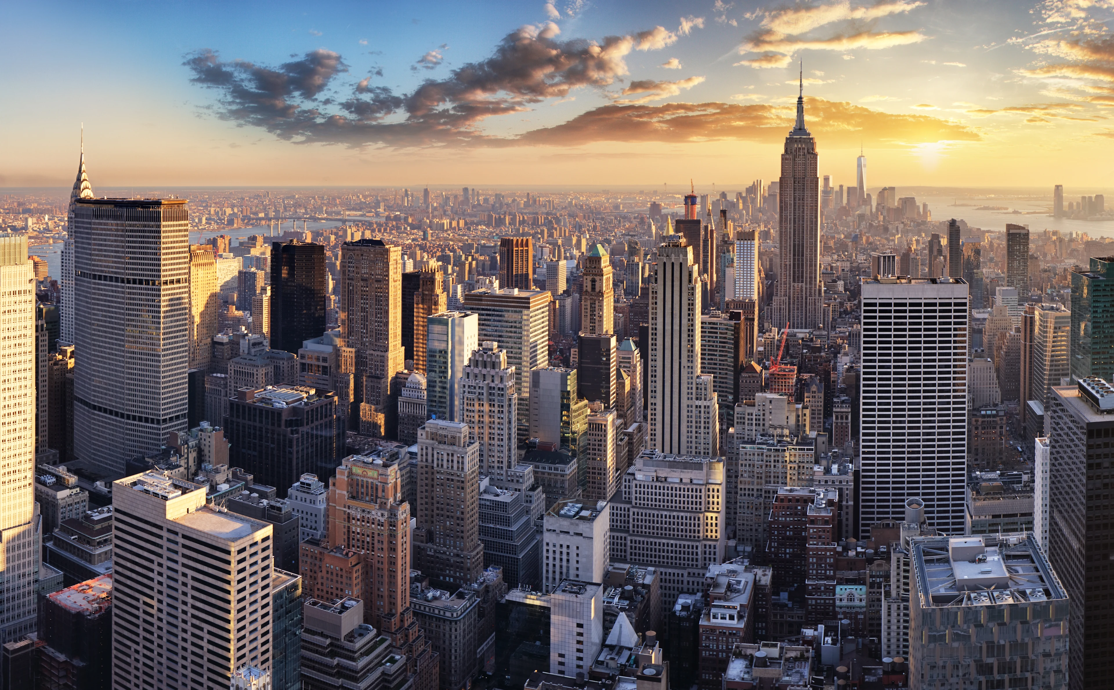 Udsigt over New Yorks skyline med Empire State Building i solnedgang.