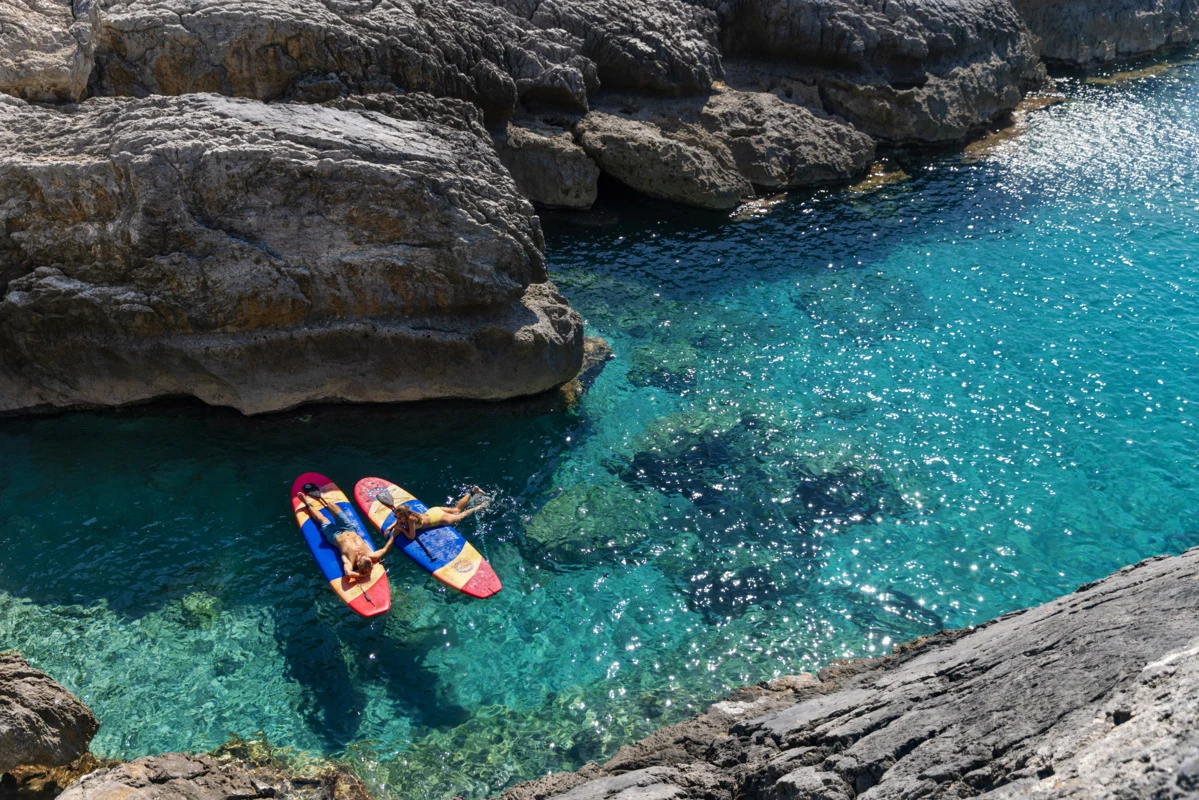 Two persons relaxing close together on a SUP each in the blue ocean