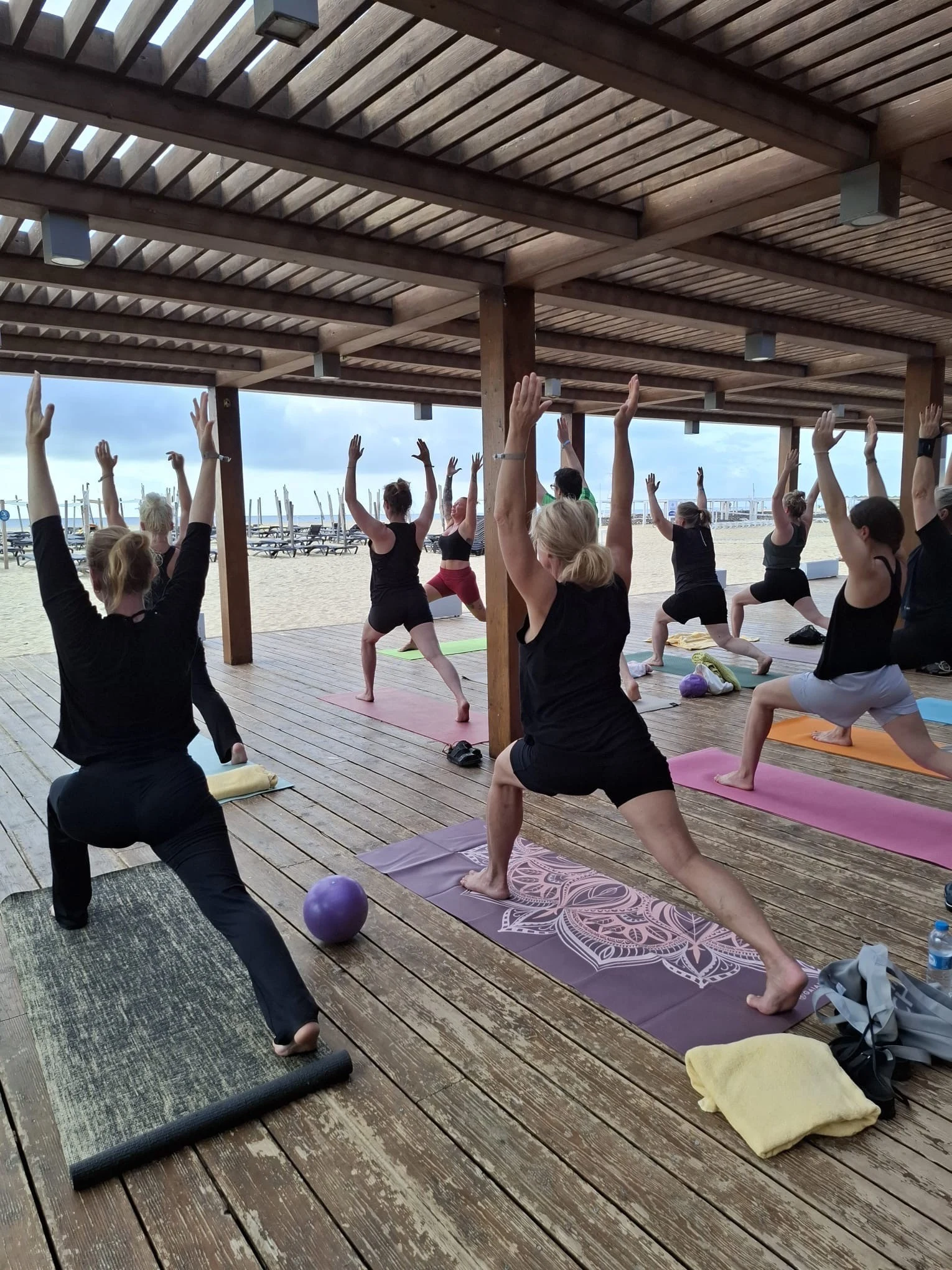 Yogaövning i grupp på en terrass med utsikt över stranden och havet.