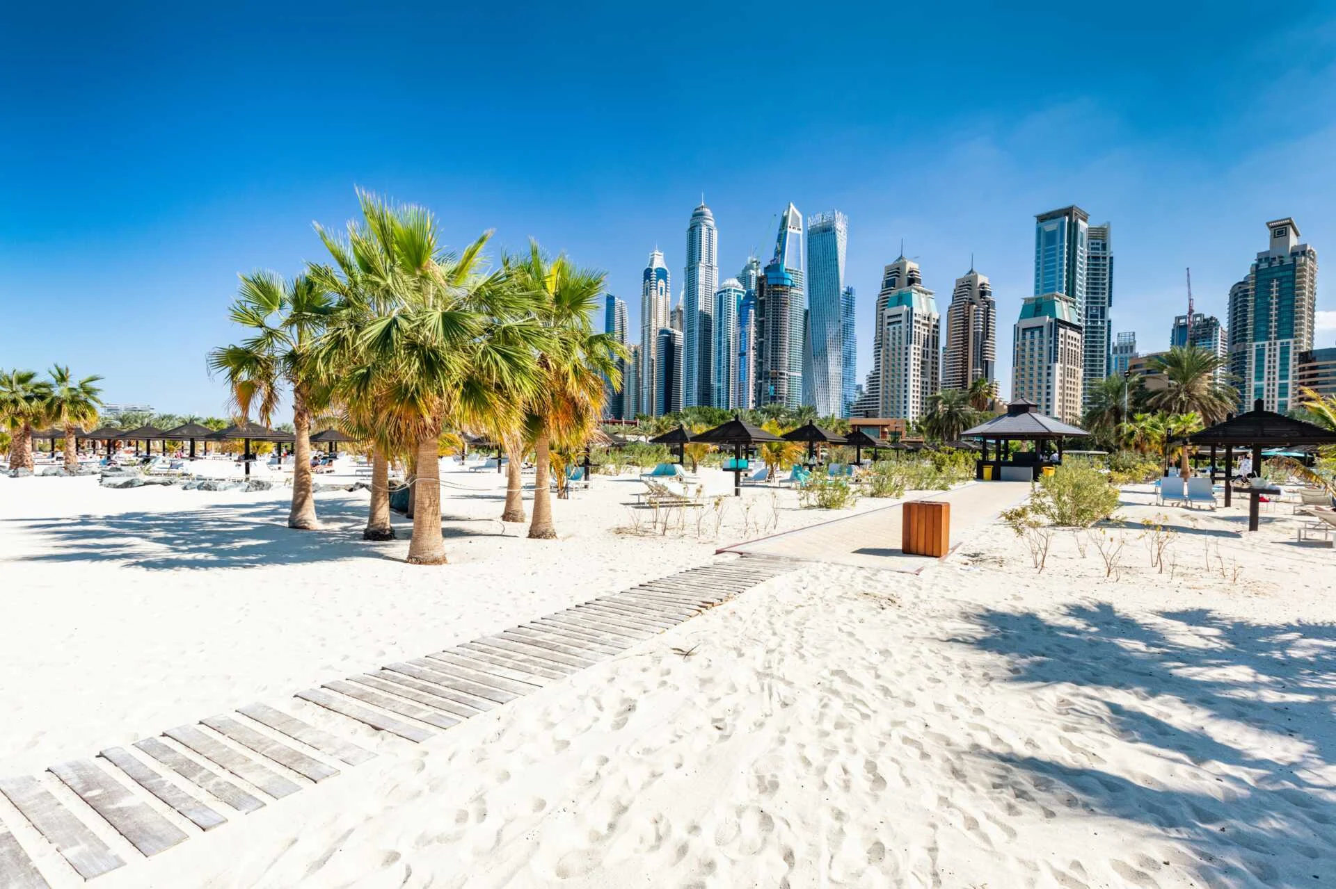 Strand i Dubai med palmer och moderna skyskrapor i bakgrunden.