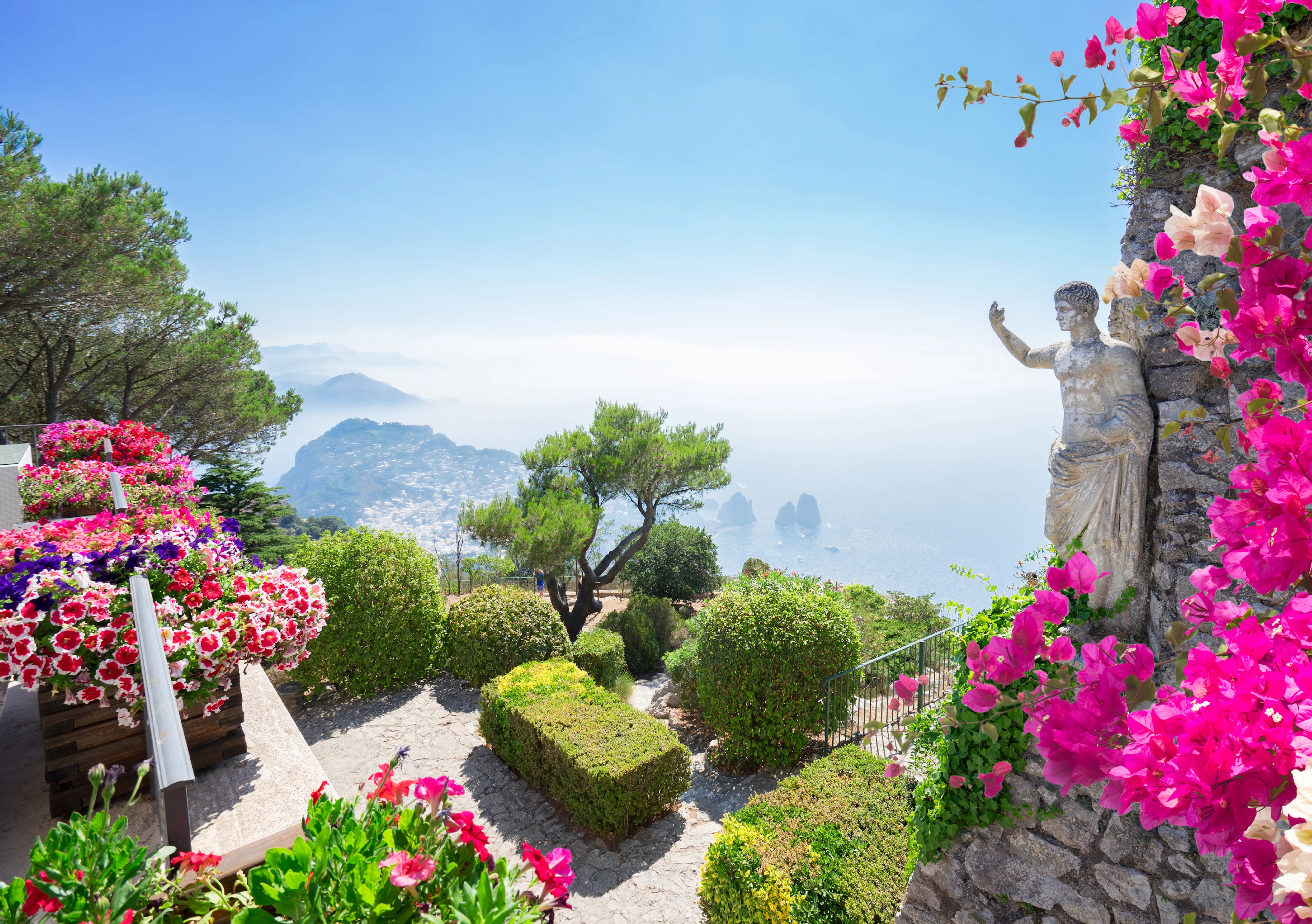 Lyserøde blomster, en statue i midten og en magisk udsigt over det glitrende hav fra Solaro på Capri