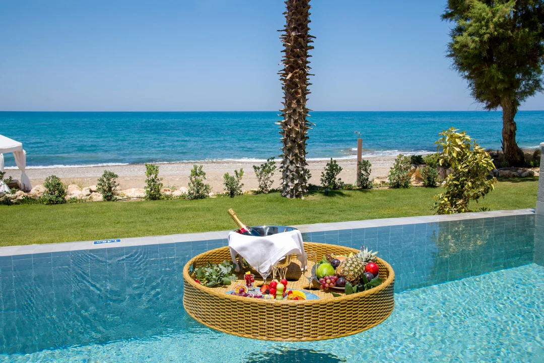 Frokostbrett i bassenget med utsikt over sandstranden og det turkise havet ved et hotell på Kreta.