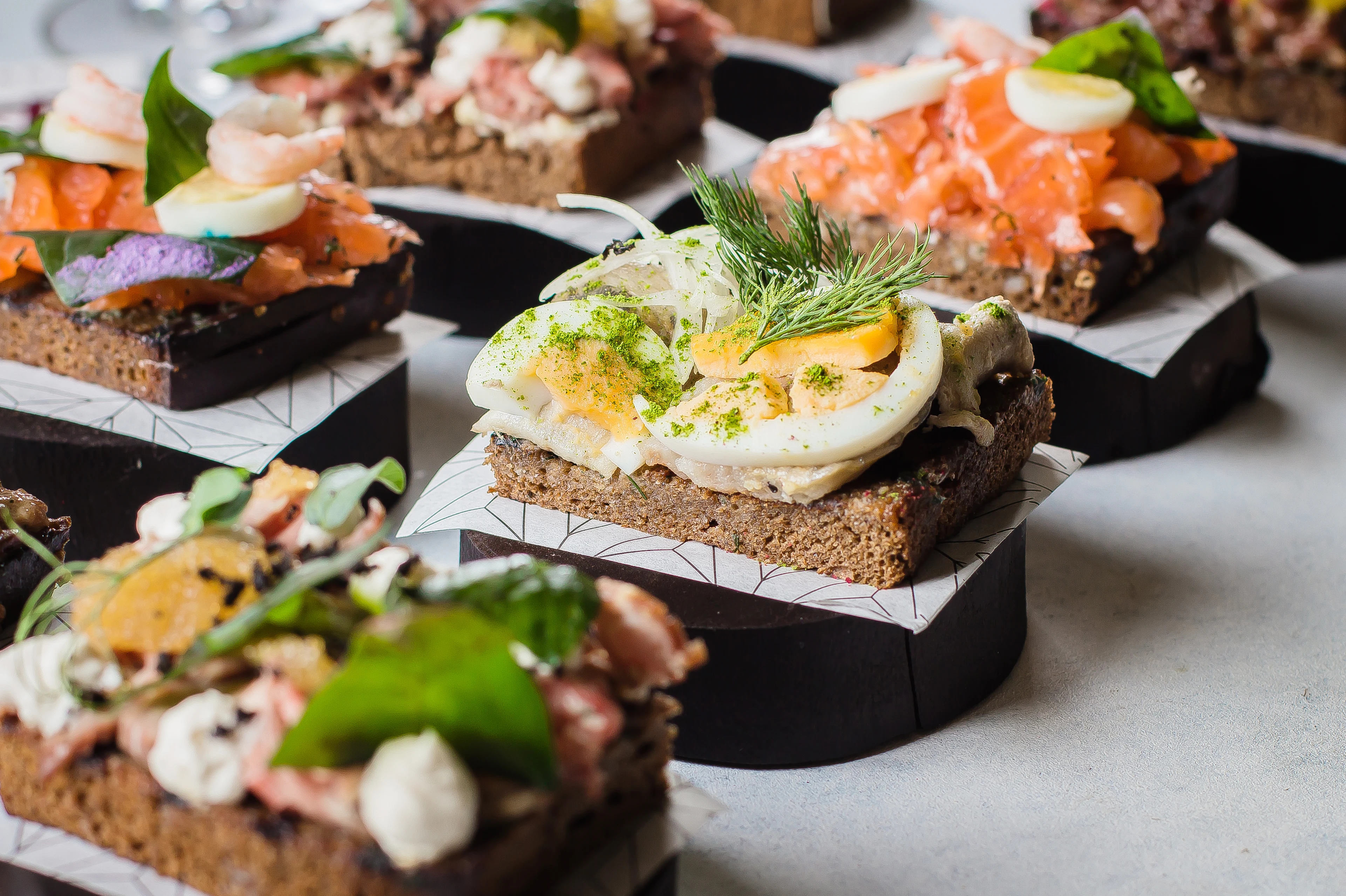 Danska smørrebröd med olika toppings, bland annat ägg, lax, räkor och färska örter, upplagda på rågbröd.