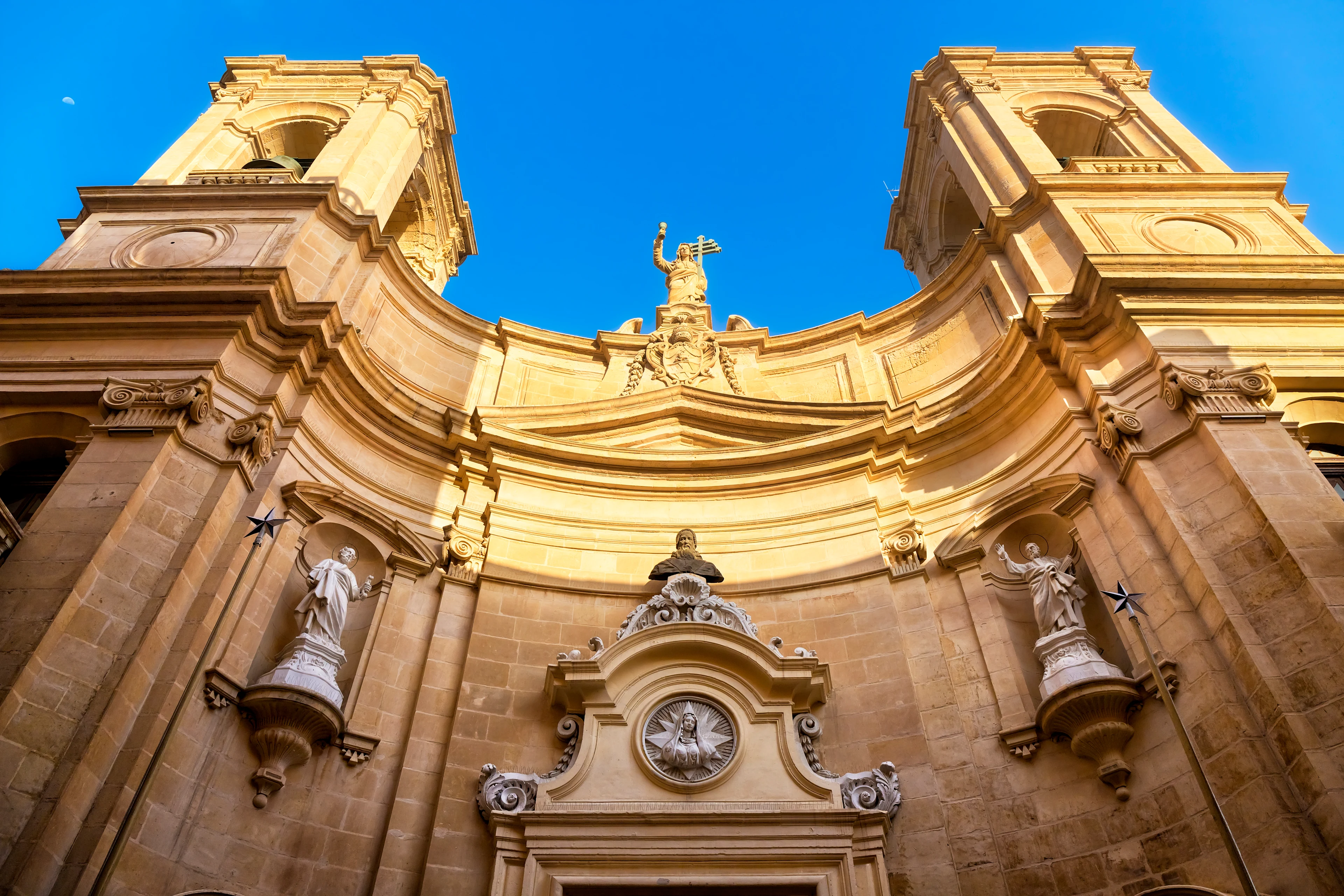 Barockfasaden på St. John's Co-Cathedral i Valletta på Malta med höga klocktorn, skulpturer och ljus kalksten mot klarblå himmel.