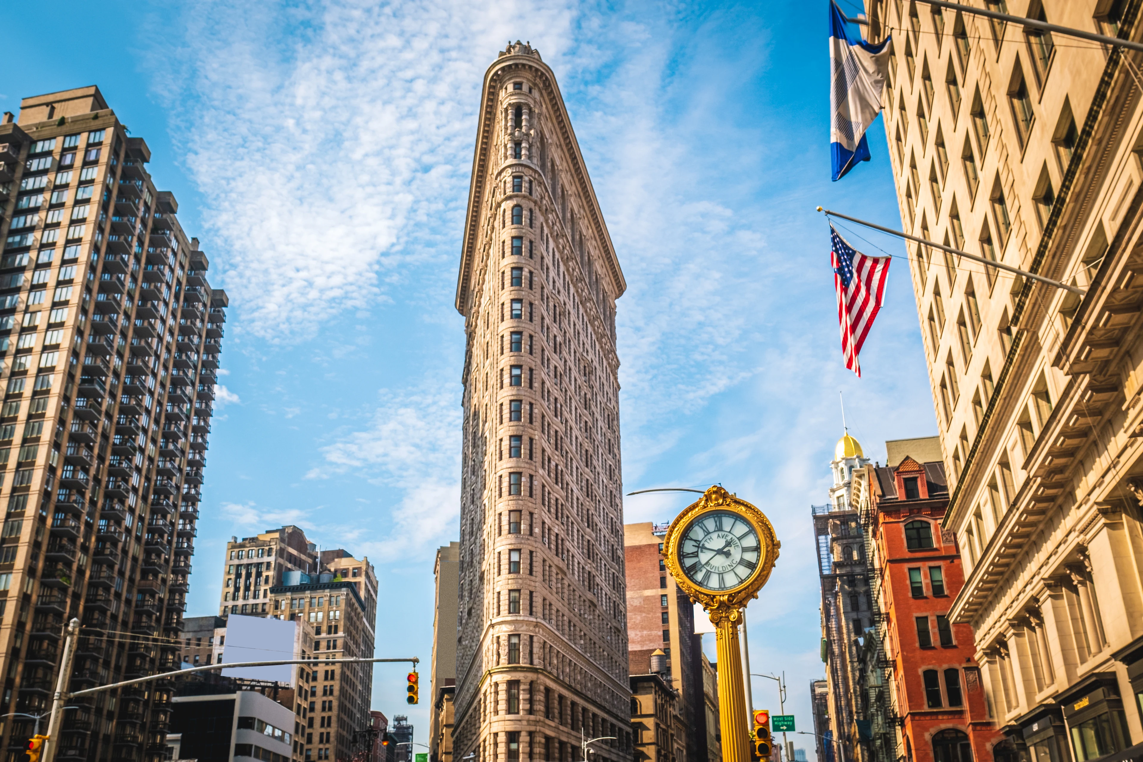 Flatiron Building i New York fotograferad från gatunivå, omgiven av höga byggnader under en blå himmel.
