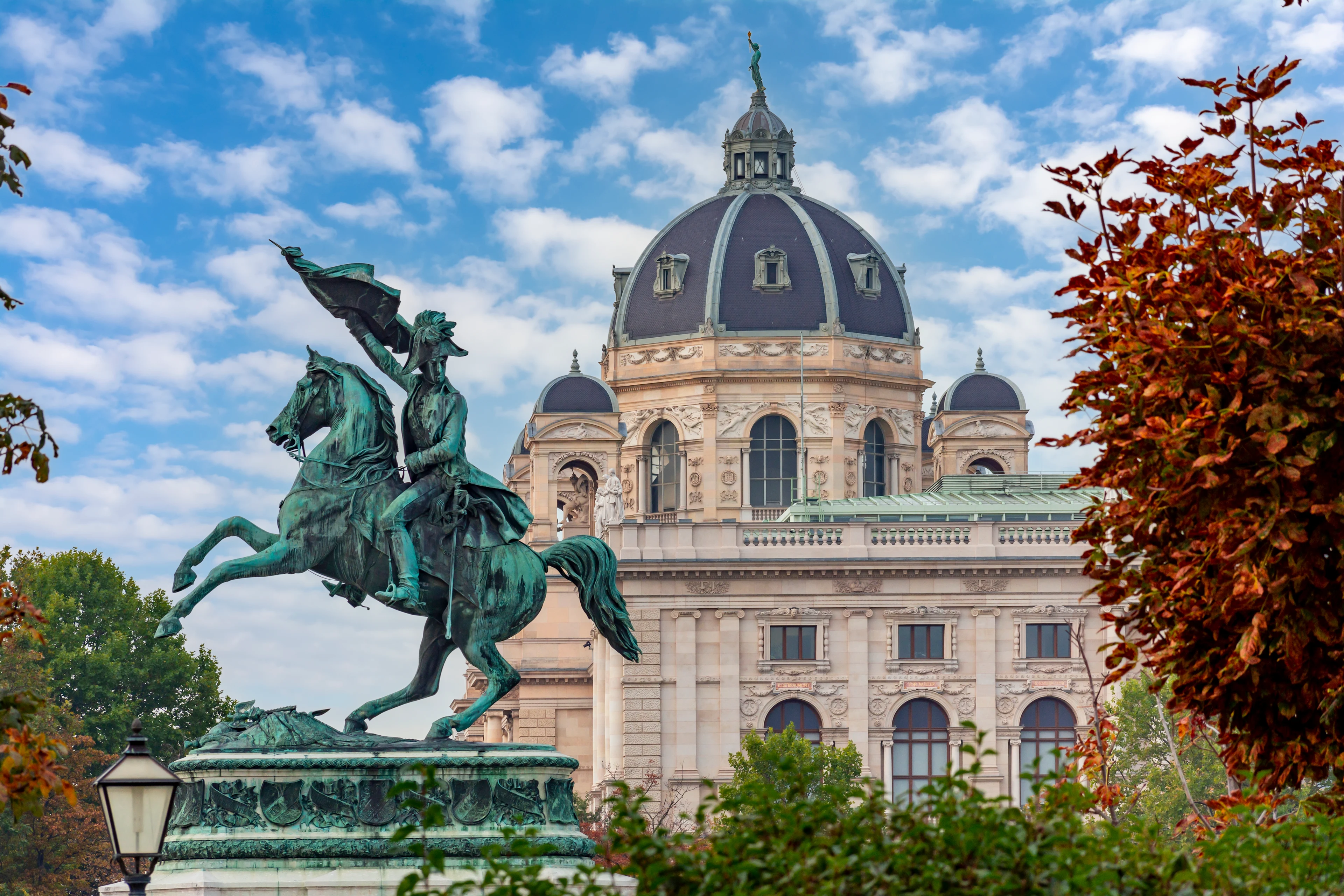 Ryttarstaty framför Konsthistoriska museet i Wien, omgiven av höstfärgade träd och historisk arkitektur.