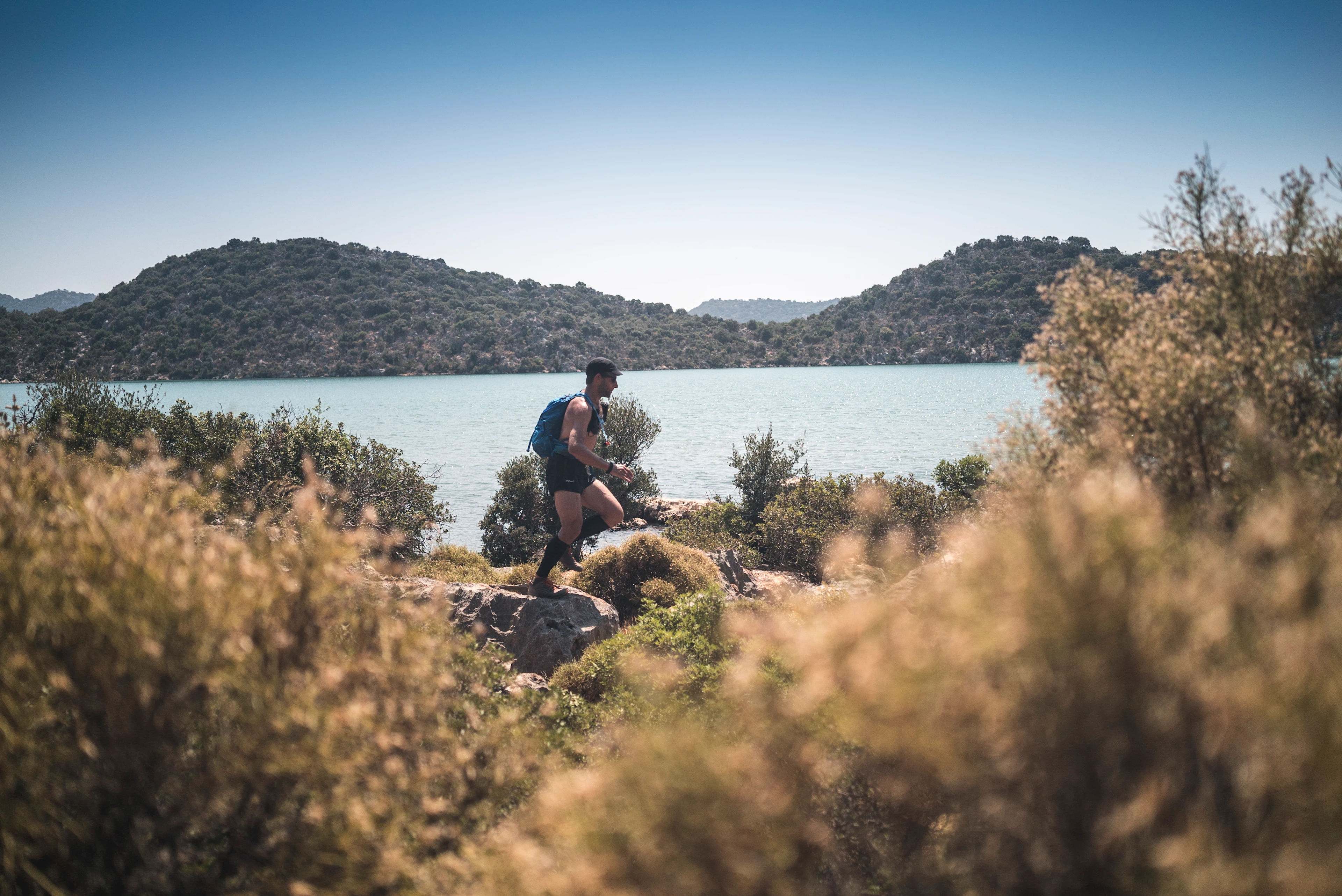 En person som løper langs en steinete sti ved en innsjø, med skogkledde åser i bakgrunnen